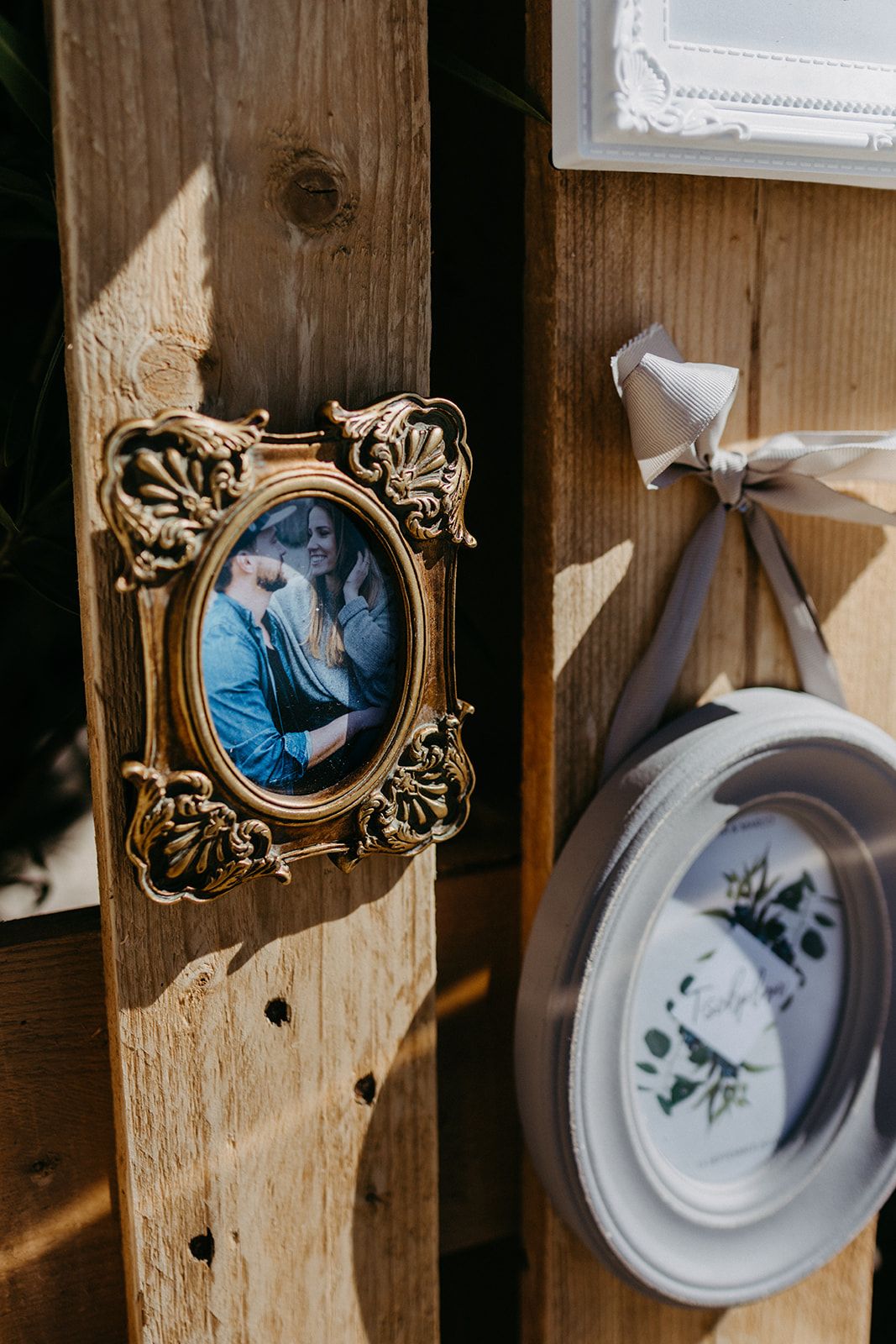 Ornate gold oval picture frame with couple photo displayed on wooden pallet wedding backdrop.