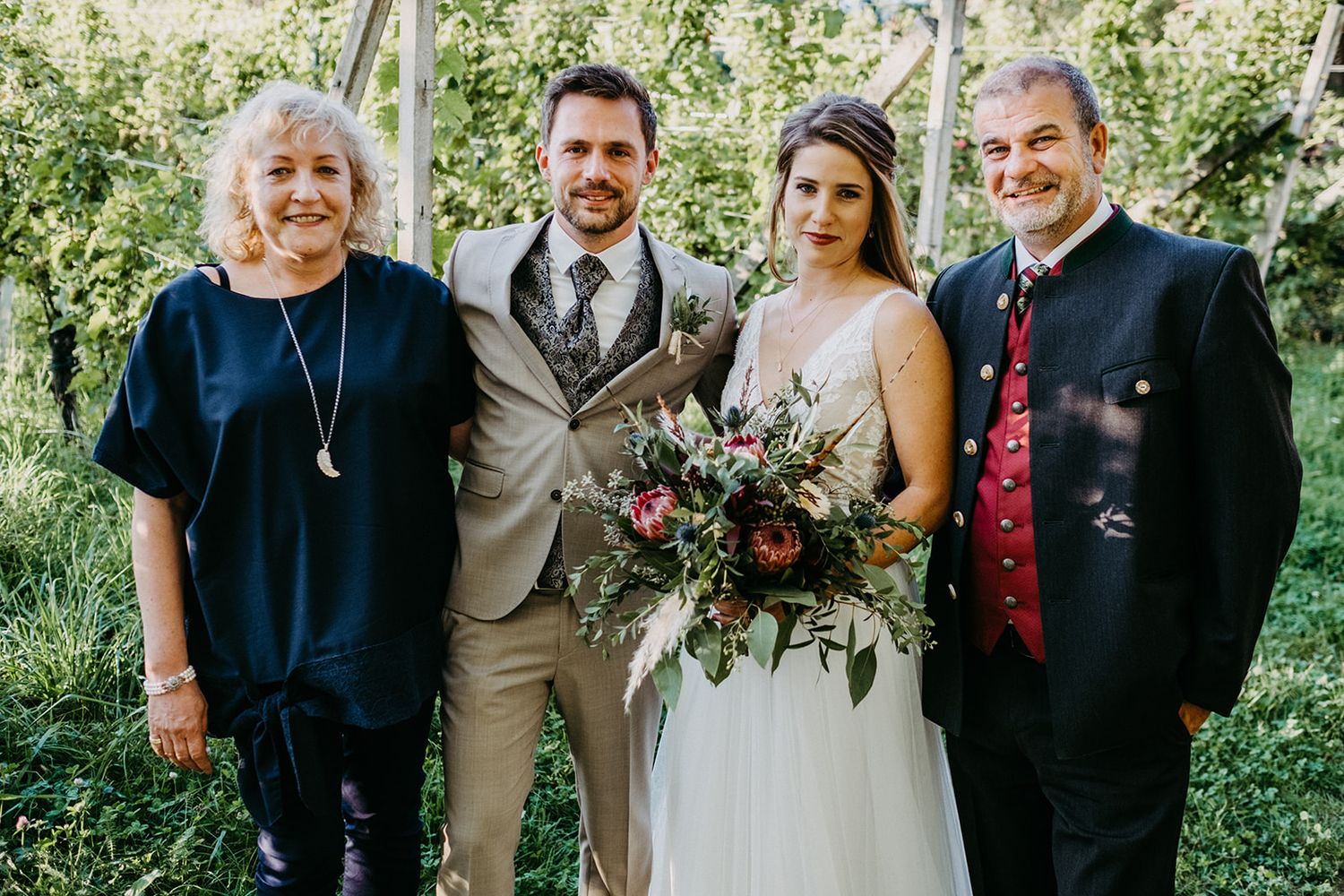 Bride and groom posing with family members in an apple orchard, bride holding a lush floral bouquet.