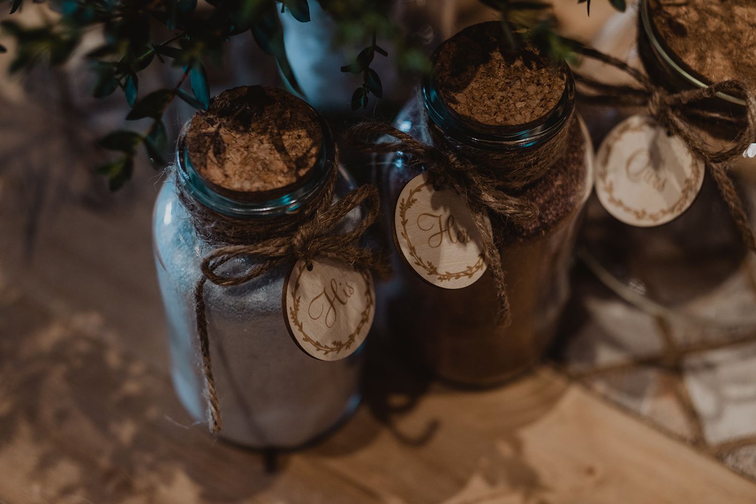 Rustic wedding favor jars with cork lids, twine, and kraft paper tags on a wooden surface.