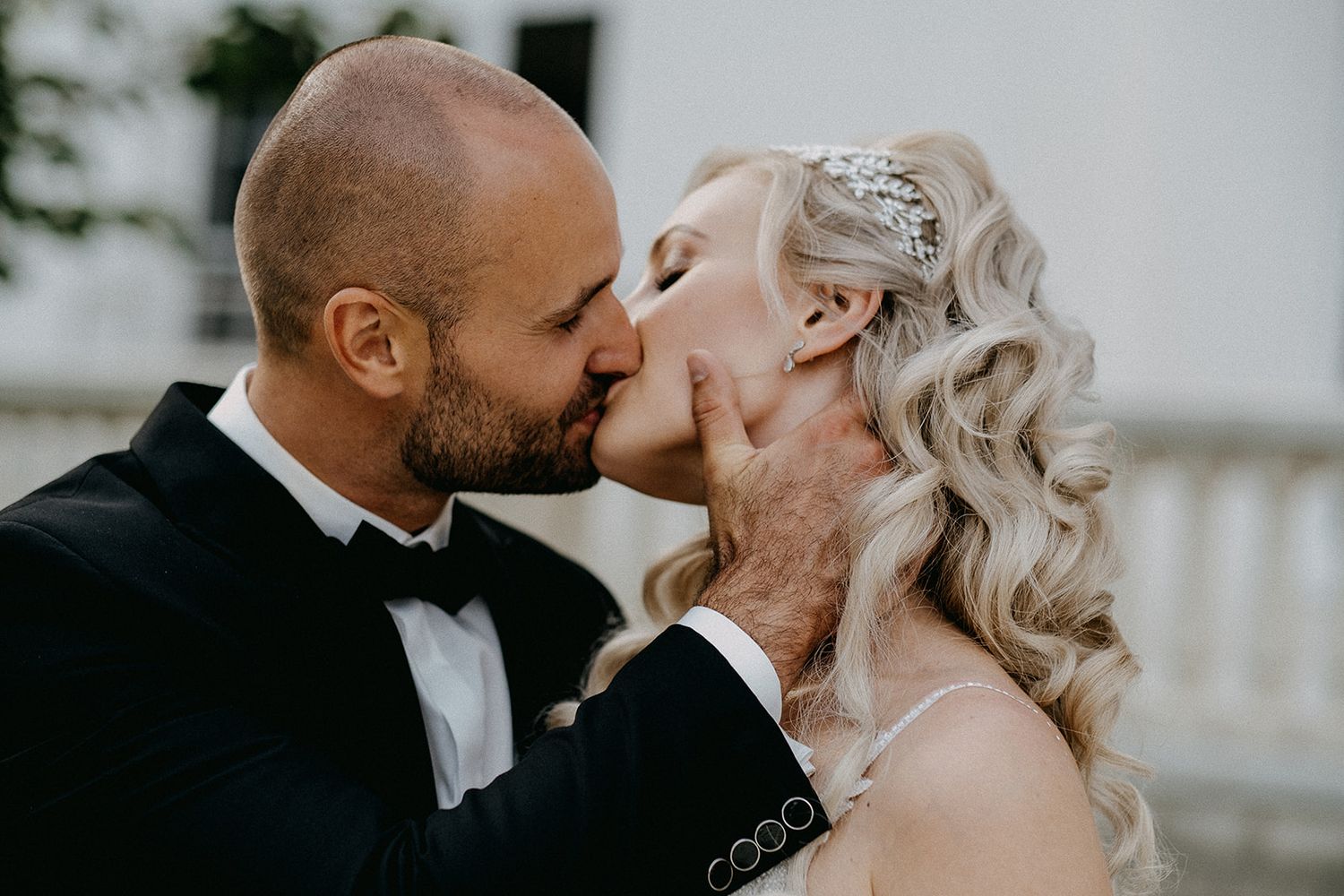 Bride and groom share passionate kiss in close-up portrait at outdoor wedding venue.
