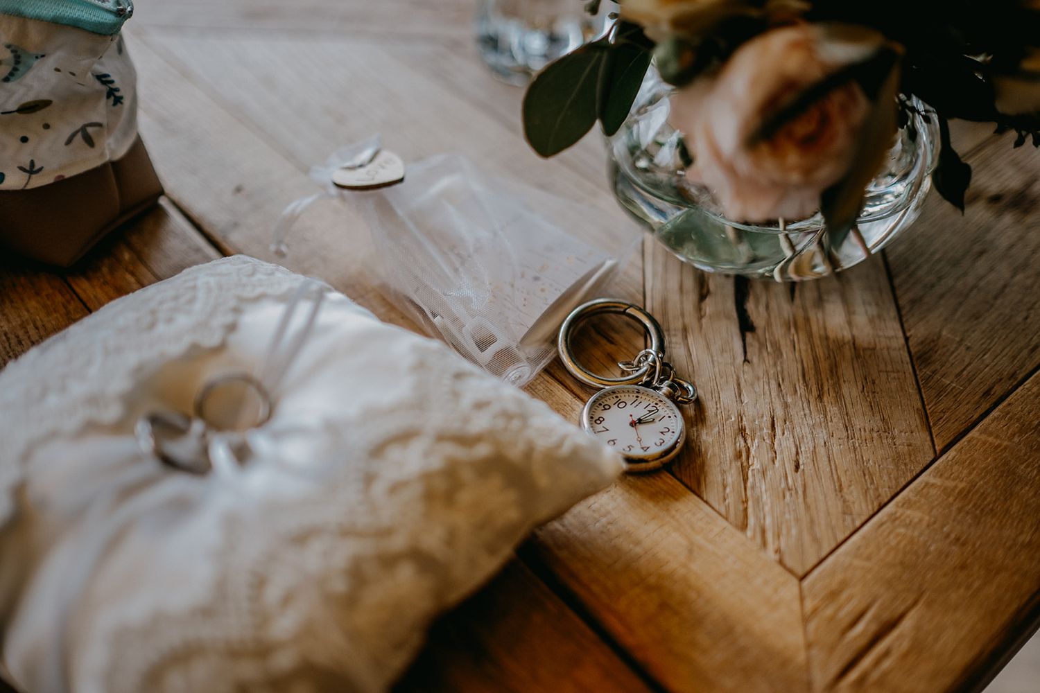 Wedding rings, pocket watch, and ring pillow on rustic wooden table.