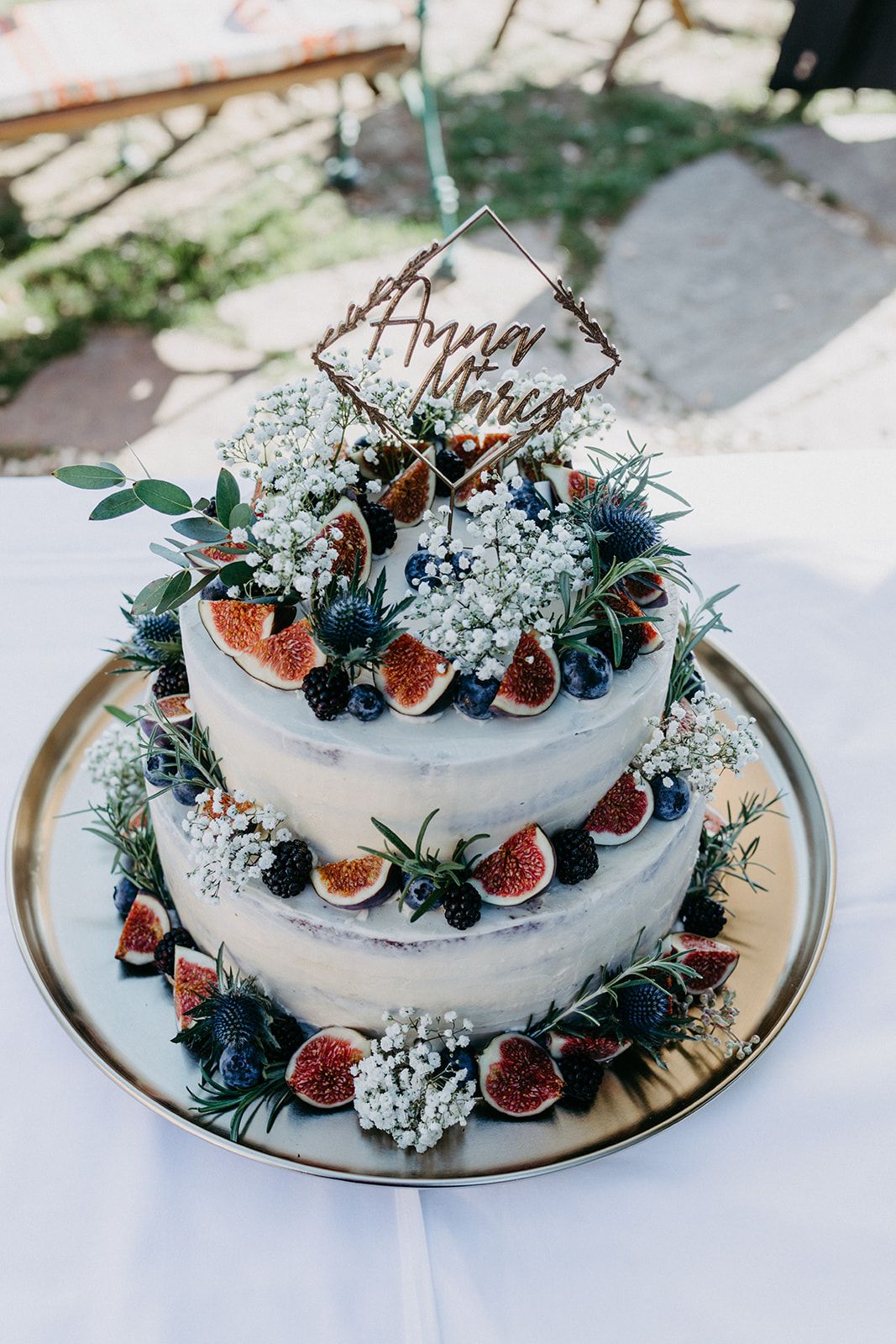 Two-tier naked wedding cake decorated with fresh figs, blueberries, blackberries, and a personalized topper.