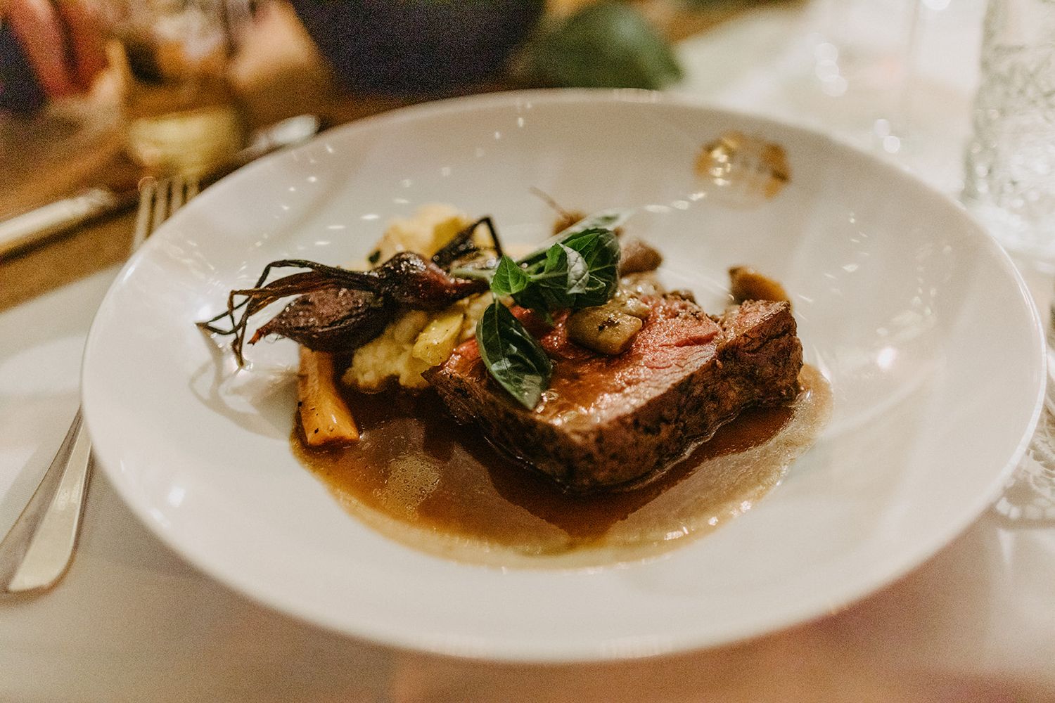 Elegant plated main course with braised meat, mushrooms, and greens served at a wedding reception.