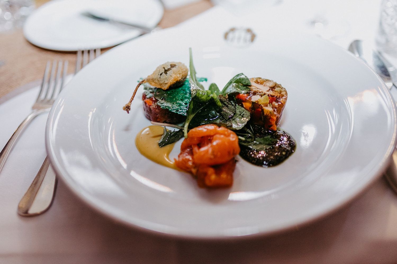 Gourmet wedding reception main course dish with roasted vegetables and greens on a white plate.