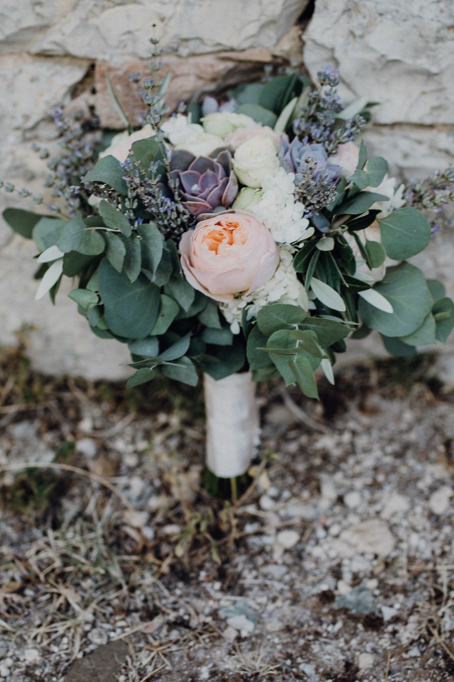 Romantic bridal bouquet with peonies, succulents, lavender, and eucalyptus against stone wall. Tuscany Villa Catignano