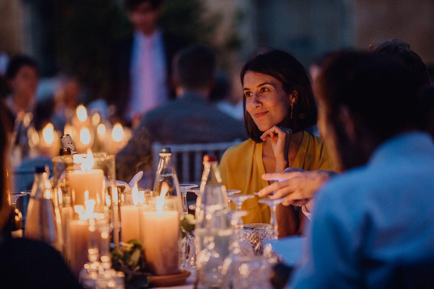 Woman in gold dress seated at candlelit outdoor wedding dinner table at dusk. Tuscany Villa Catignano