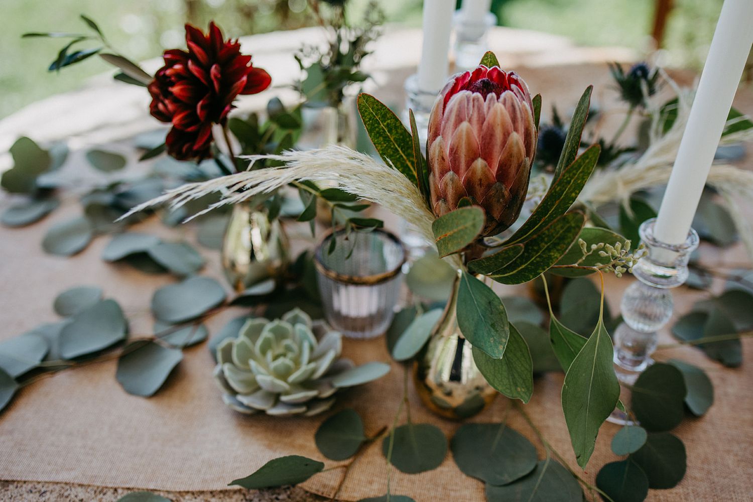 Rustic wedding table centerpiece with protea, succulents, eucalyptus and gold bud vases.