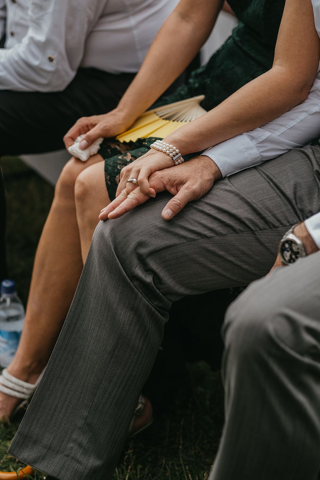 Couple holding hands with pearl bracelet and wedding ring during outdoor ceremony.
