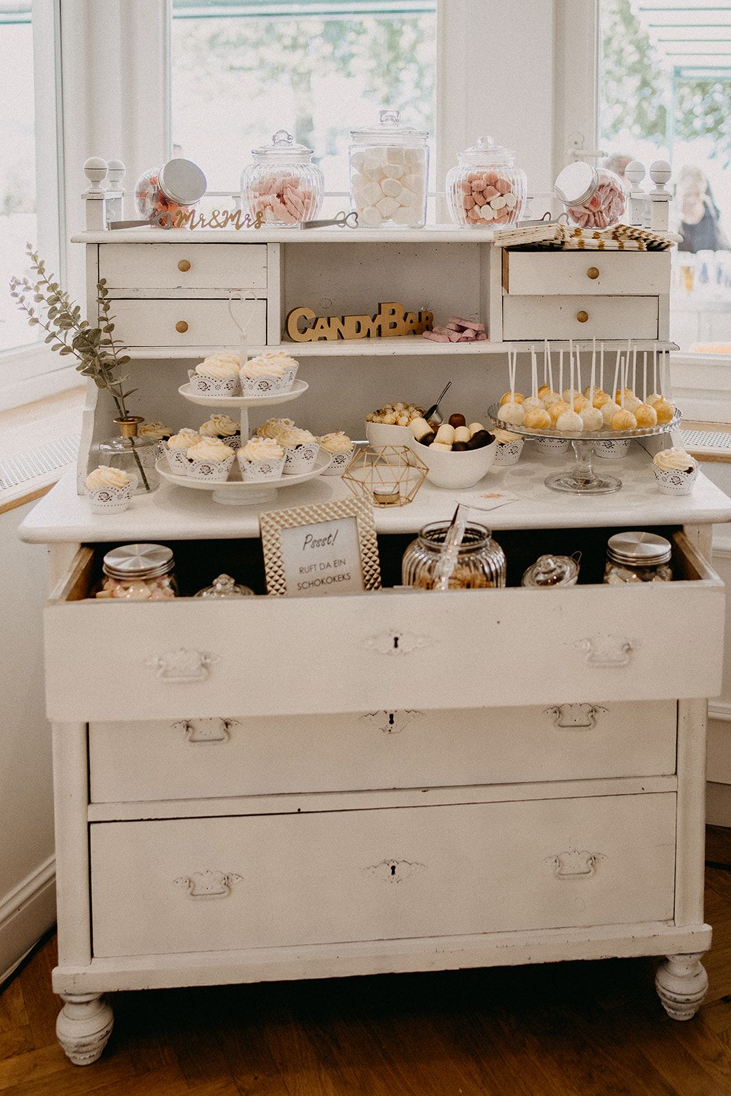 White vintage dresser styled as elegant wedding candy bar with cupcakes and cake pops.