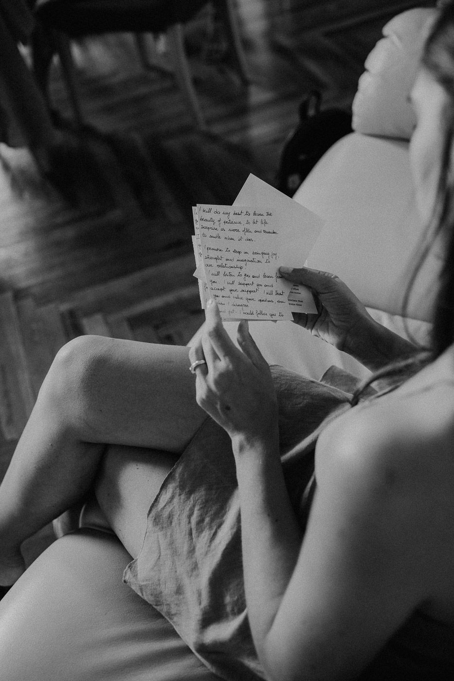 Black and white photo of a bride reading handwritten wedding vow letters while seated in a chair. Tuscany Villa Catignano