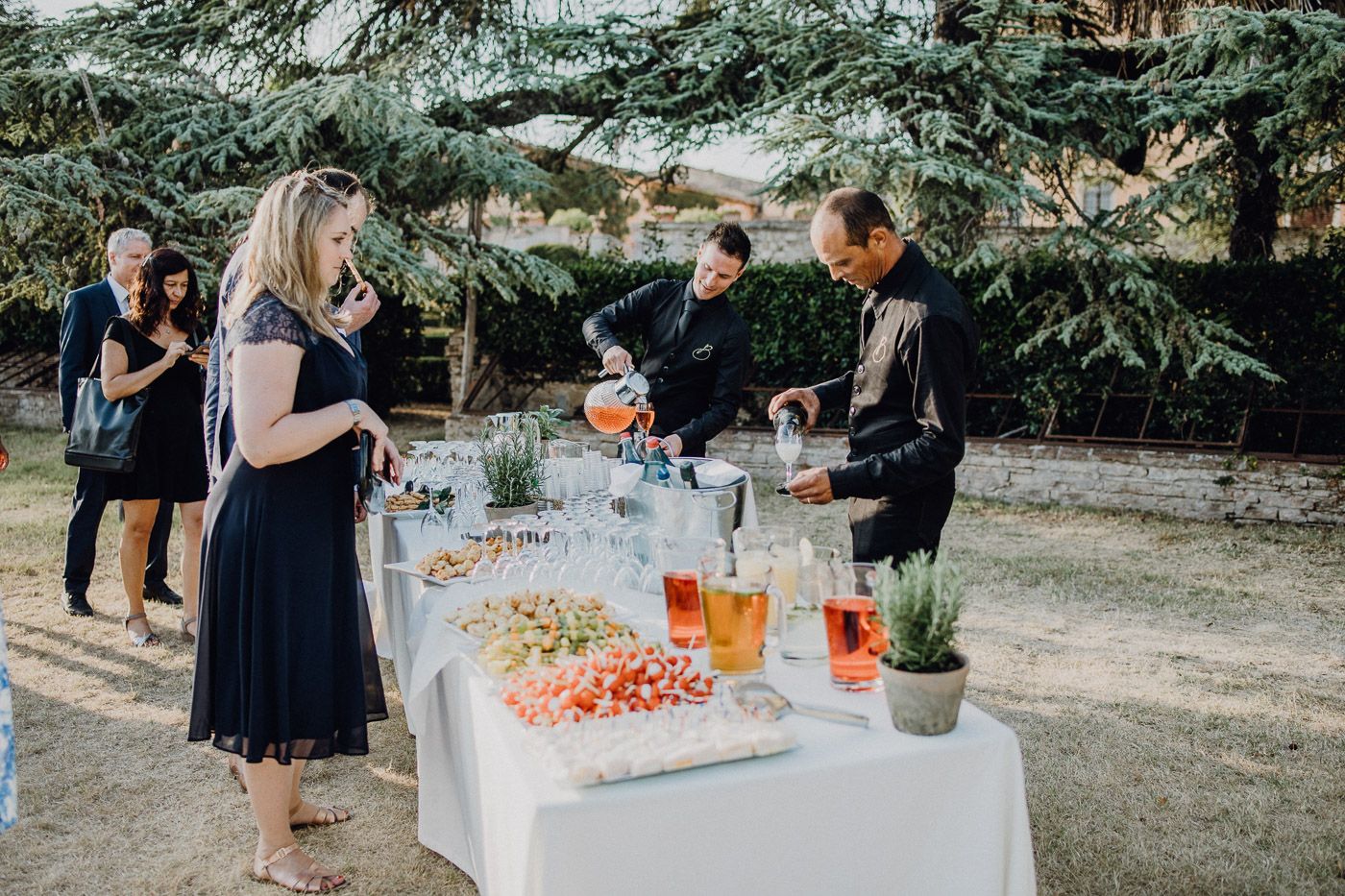 Wedding guests enjoying outdoor cocktail hour with catered food and drink station in garden. Tuscany Villa Catignano