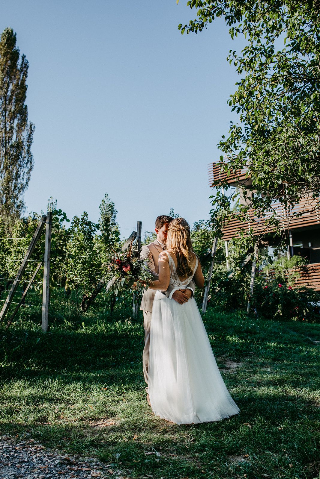 Bride and groom sharing a romantic kiss in a lush green garden during their outdoor wedding ceremony.