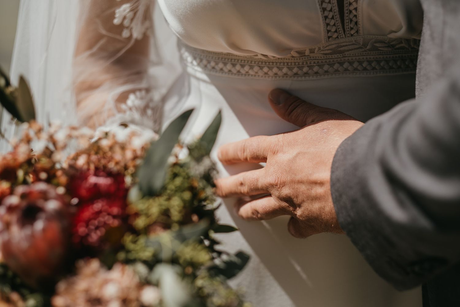 Close-up of groom placing wedding ring on brides finger beside a floral bouquet.