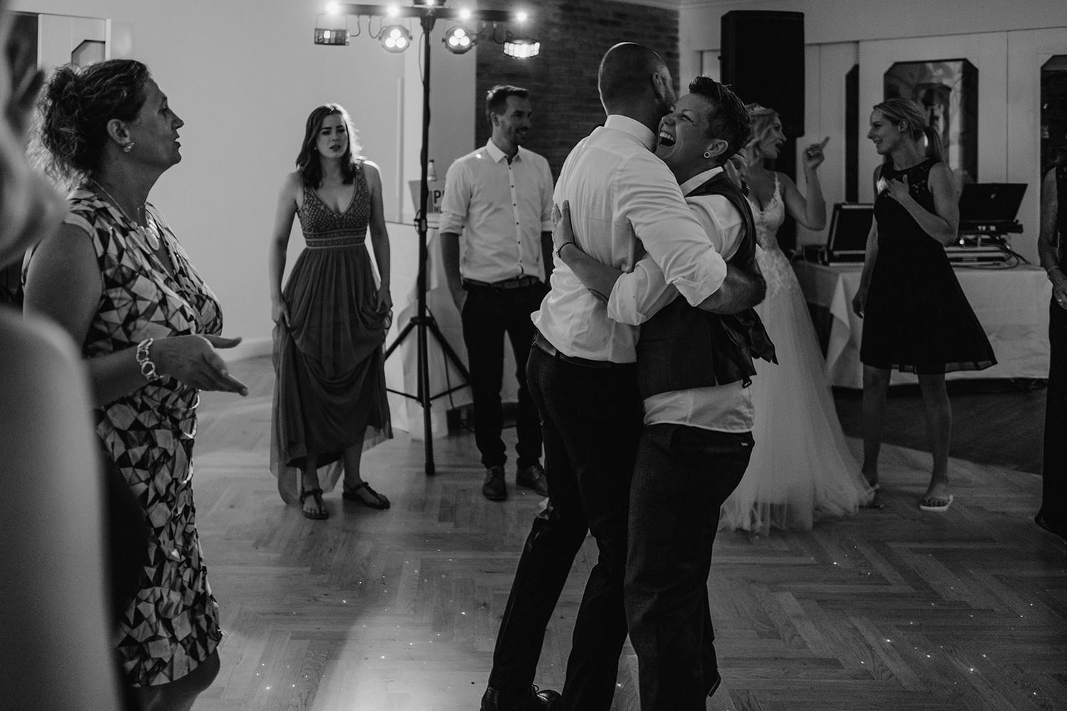 Black and white photo of wedding guests dancing and socializing on the reception dance floor.