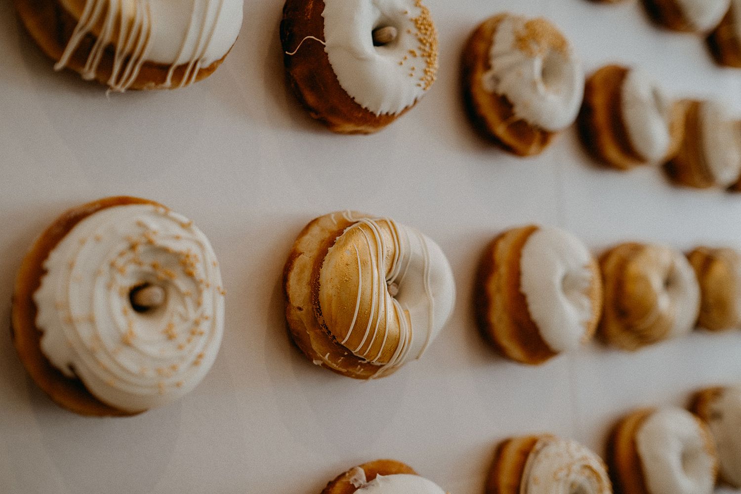 A decorative donut wall display featuring glazed and frosted donuts arranged in rows at a wedding reception.