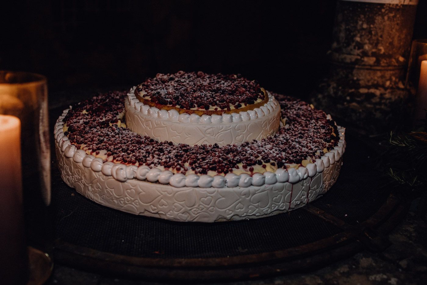 Two-tier white wedding cake topped with chocolate sprinkles displayed on a dark surface with candles. Tuscany Villa Catignano