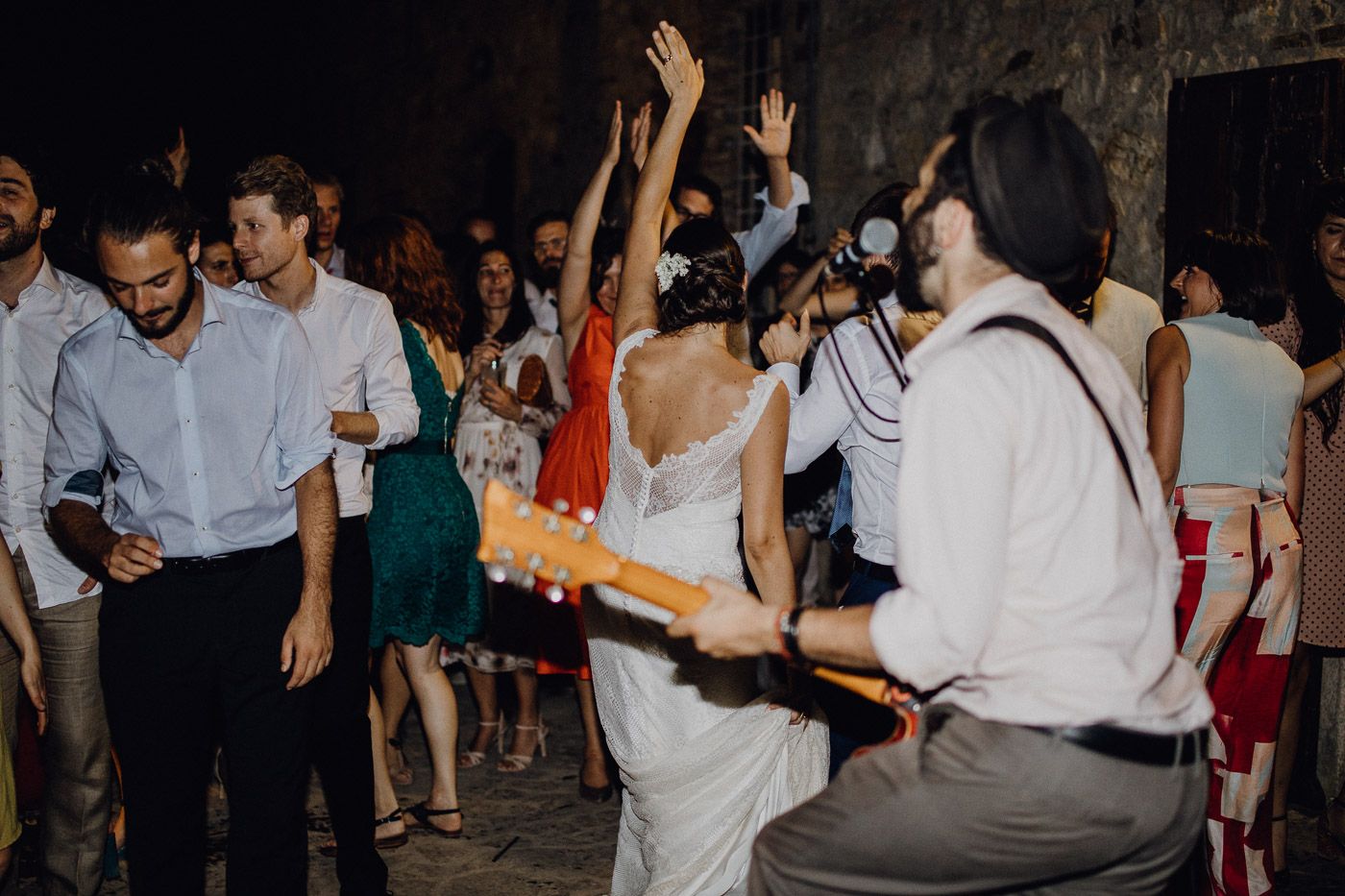 Bride in white gown dances with guests as live guitarist performs at an outdoor wedding reception. Tuscany Villa Catignano
