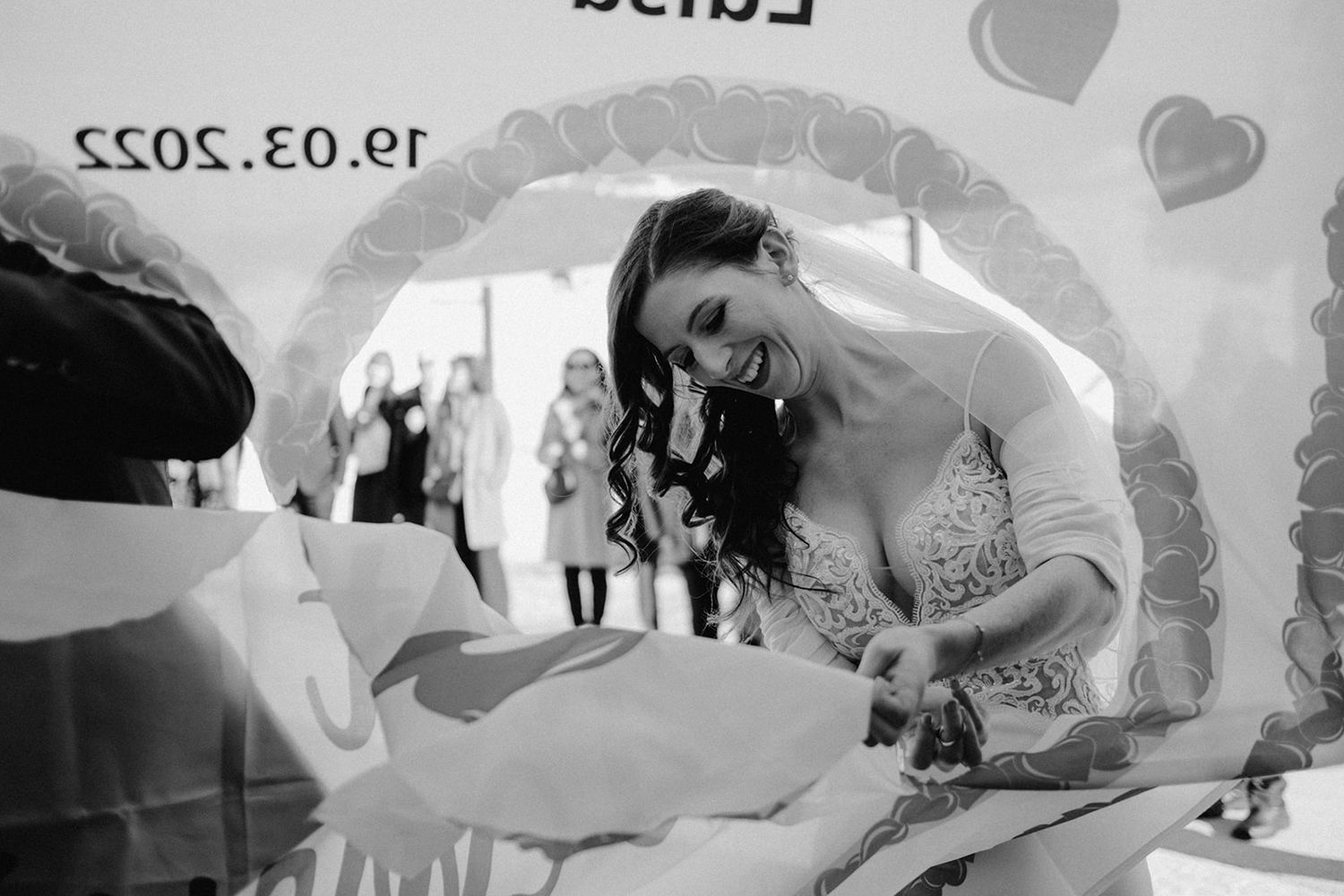 Black and white photo of joyful bride in wedding dress cutting cake at reception dated 19.03.2022. Jufenalm