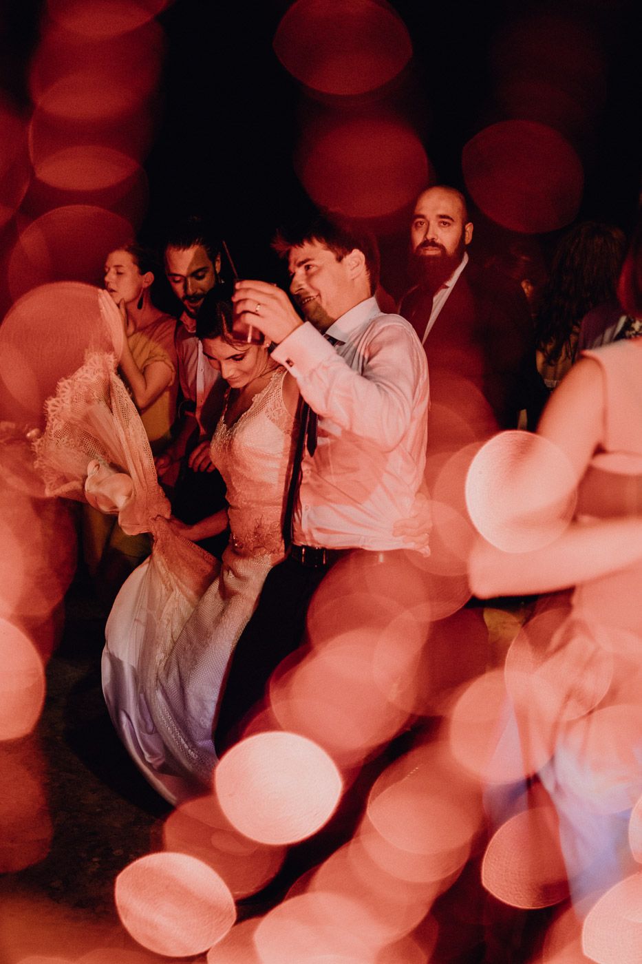 Bride and groom dancing joyfully at wedding reception surrounded by guests and warm bokeh lights. Tuscany Villa Catignano