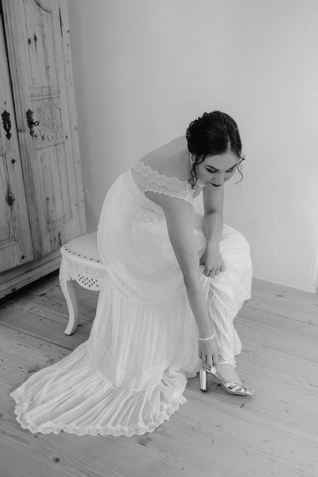 Bride in white lace wedding dress putting on heels, black and white photo.