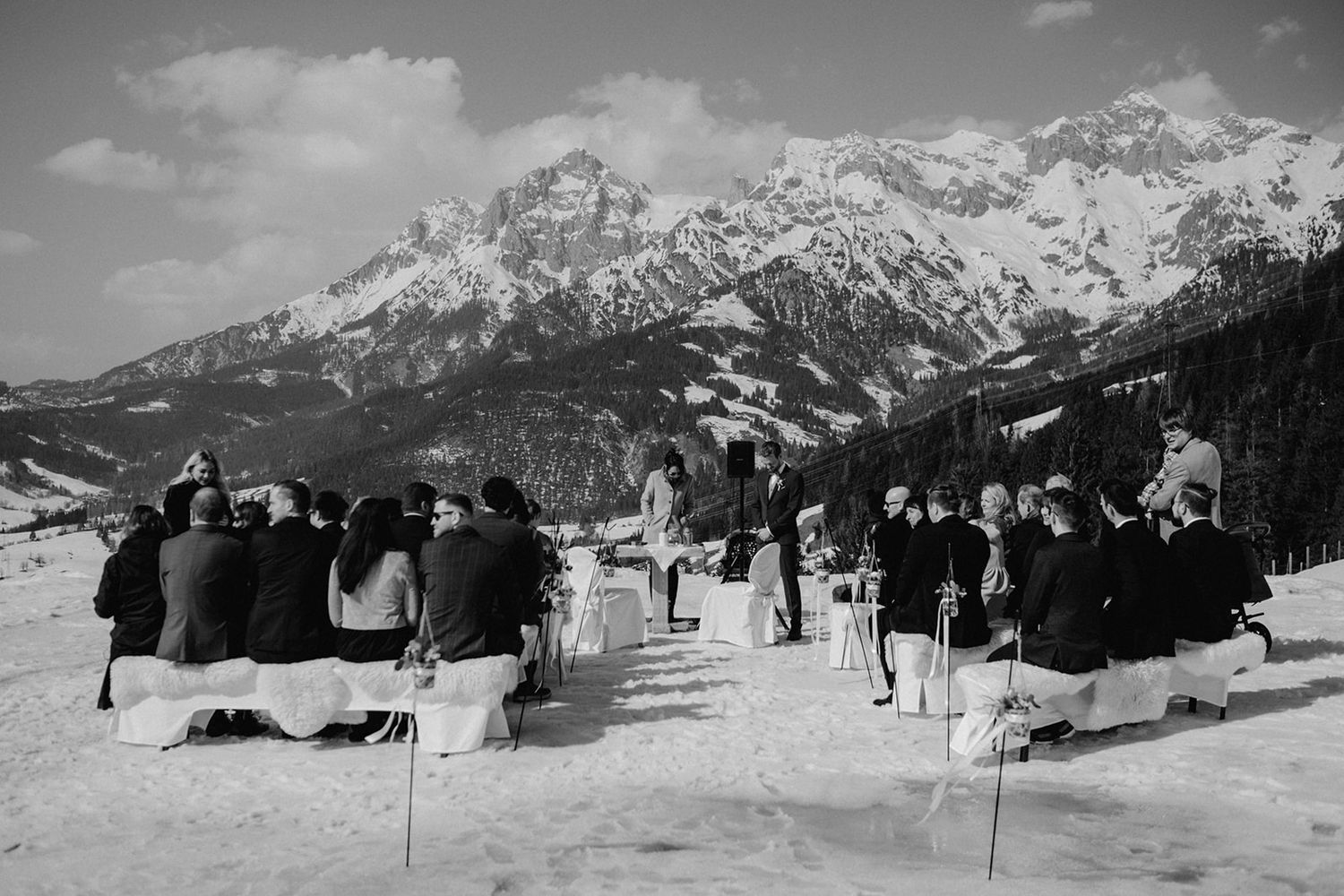 Black and white aerial view of outdoor winter wedding ceremony with snowy mountain backdrop.