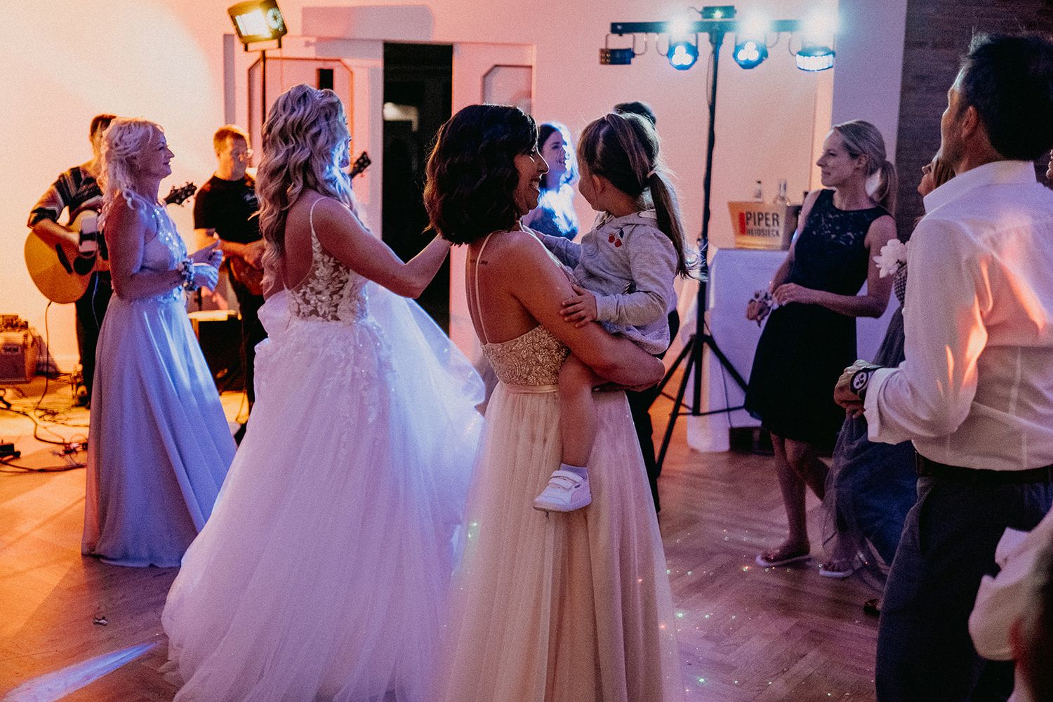Wedding guests including bridesmaids in elegant gowns dancing together on the reception dance floor.