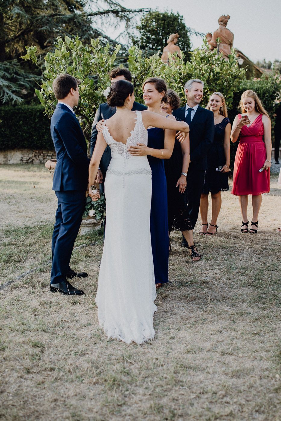Bride in lace gown embraced by bridesmaid in navy dress at outdoor wedding reception. Tuscany Villa Catignano