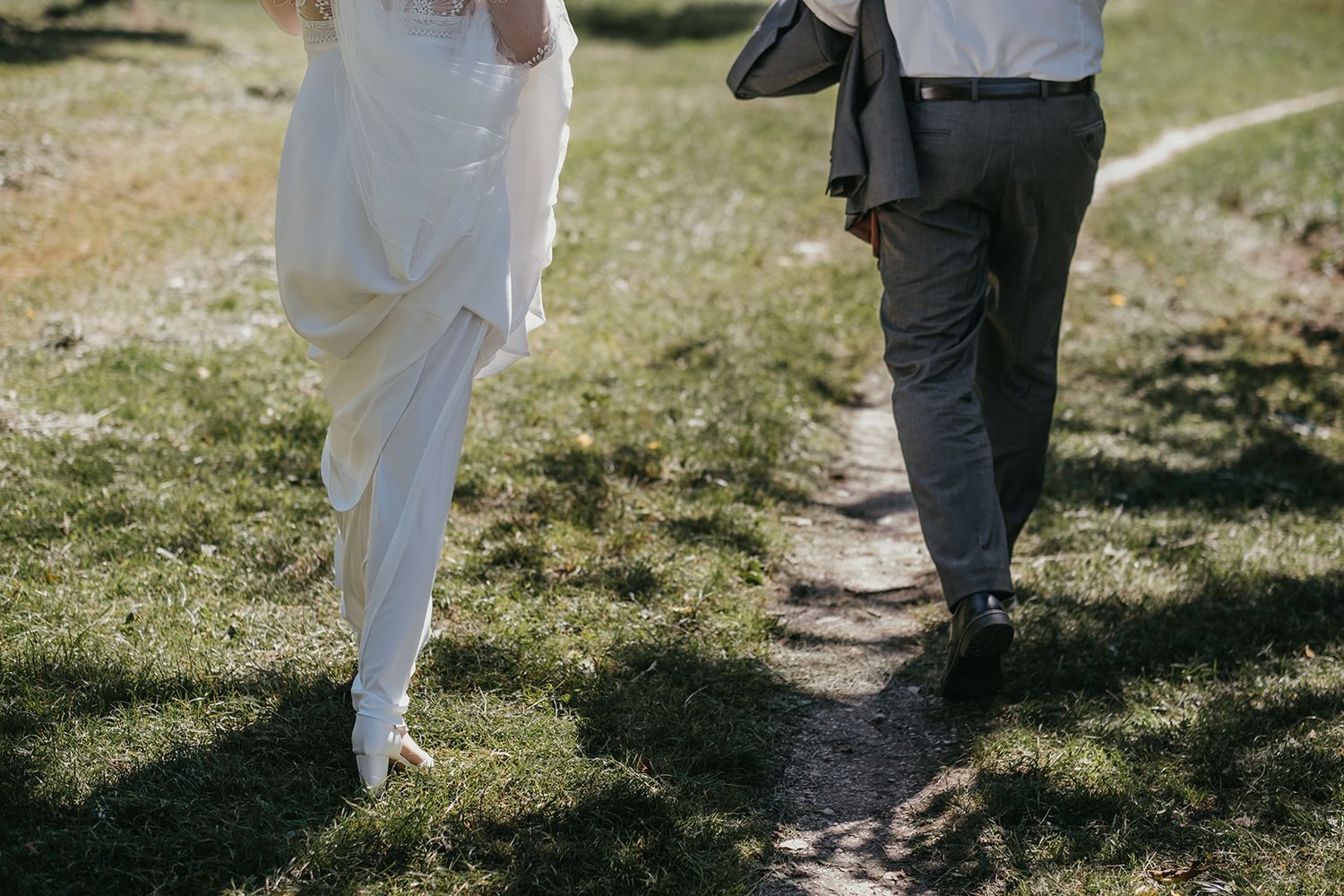 Bride and groom walking hand in hand on garden path at wedding.