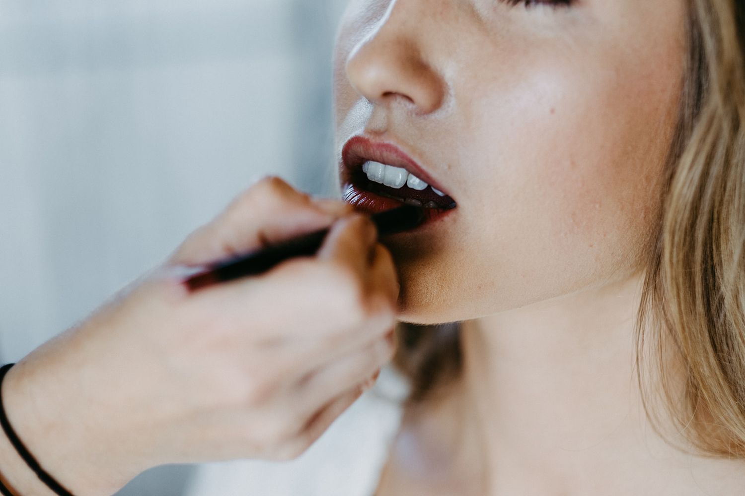 Close-up of makeup artist applying dark lipstick to bride before wedding.