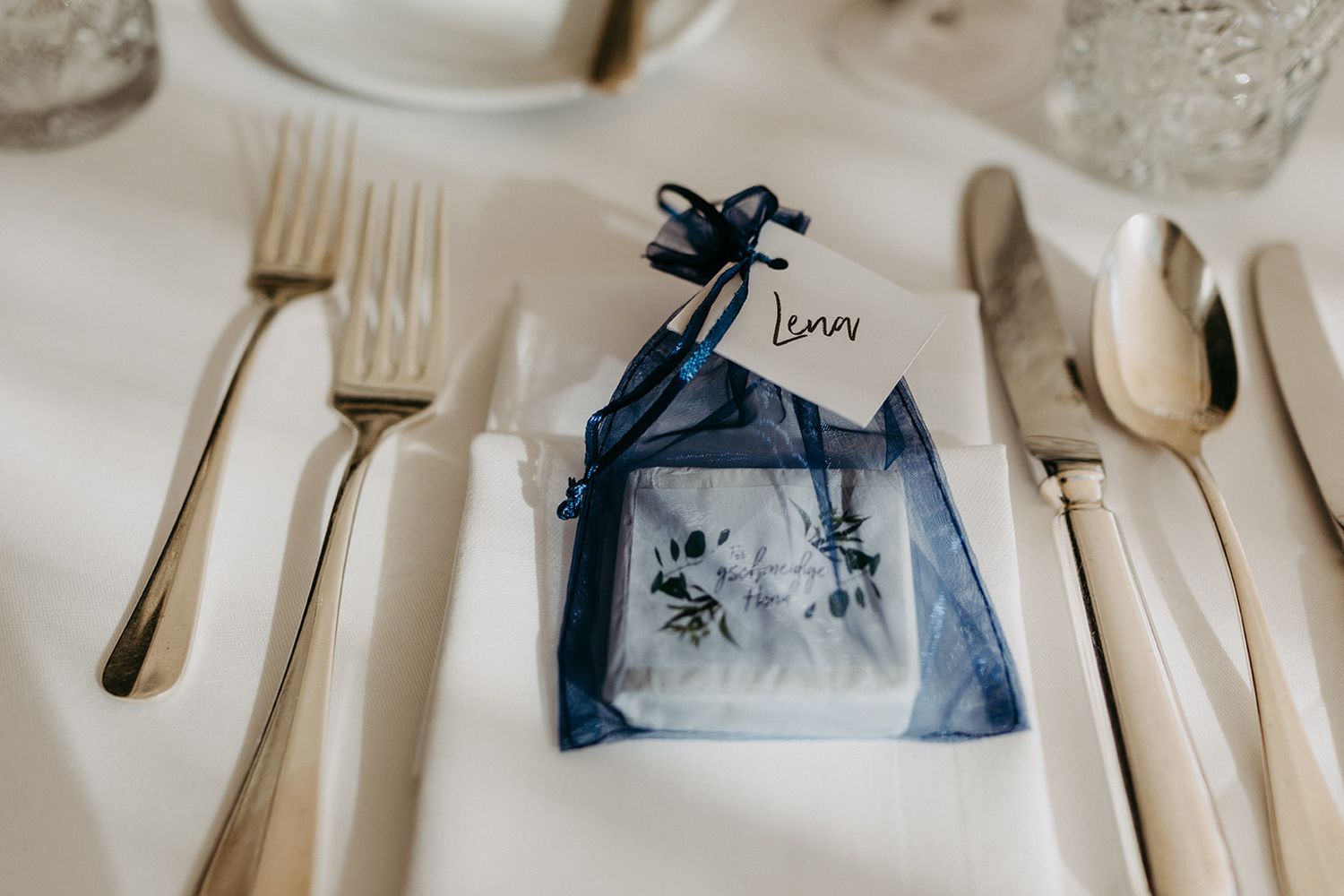 Elegant navy blue wedding favor bag with floral design and name card on white table.