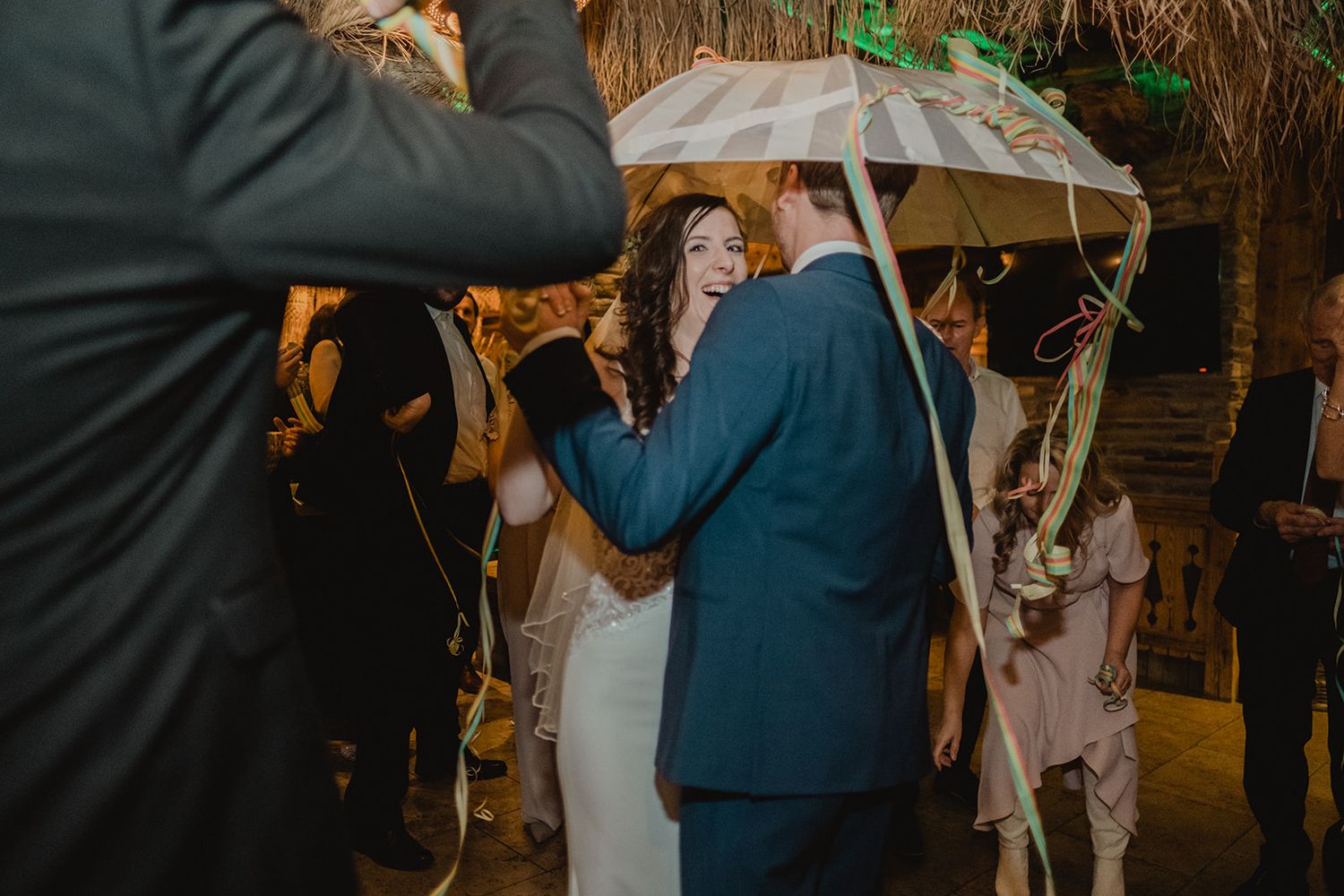 Bride and groom laughing together under a decorated umbrella during festive wedding reception celebration. Jufenalm