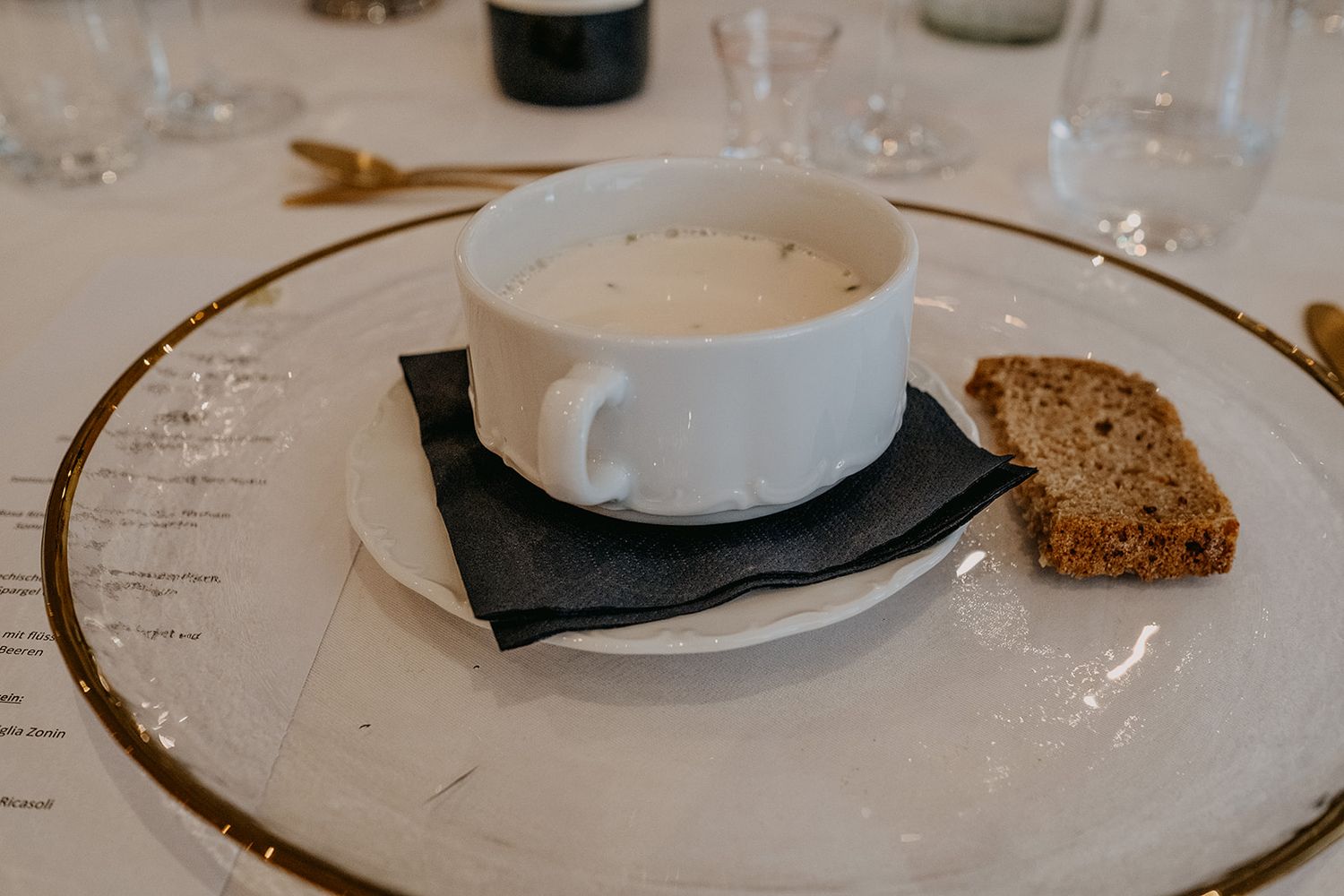 A bowl of creamy soup served with multigrain bread on a gold-rimmed white plate at a wedding.