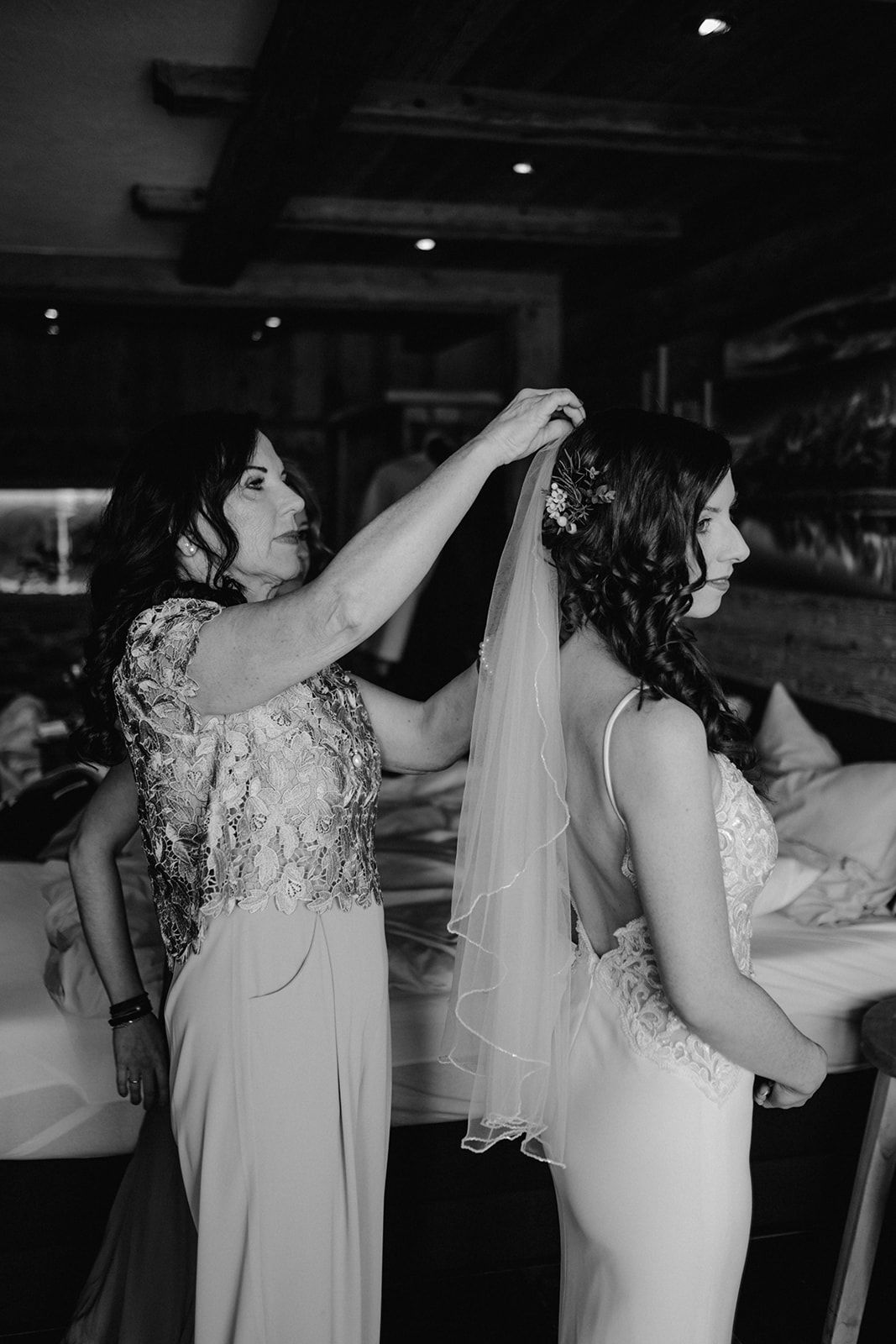 Mother helping bride attach veil to hair in black and white wedding preparation photo.