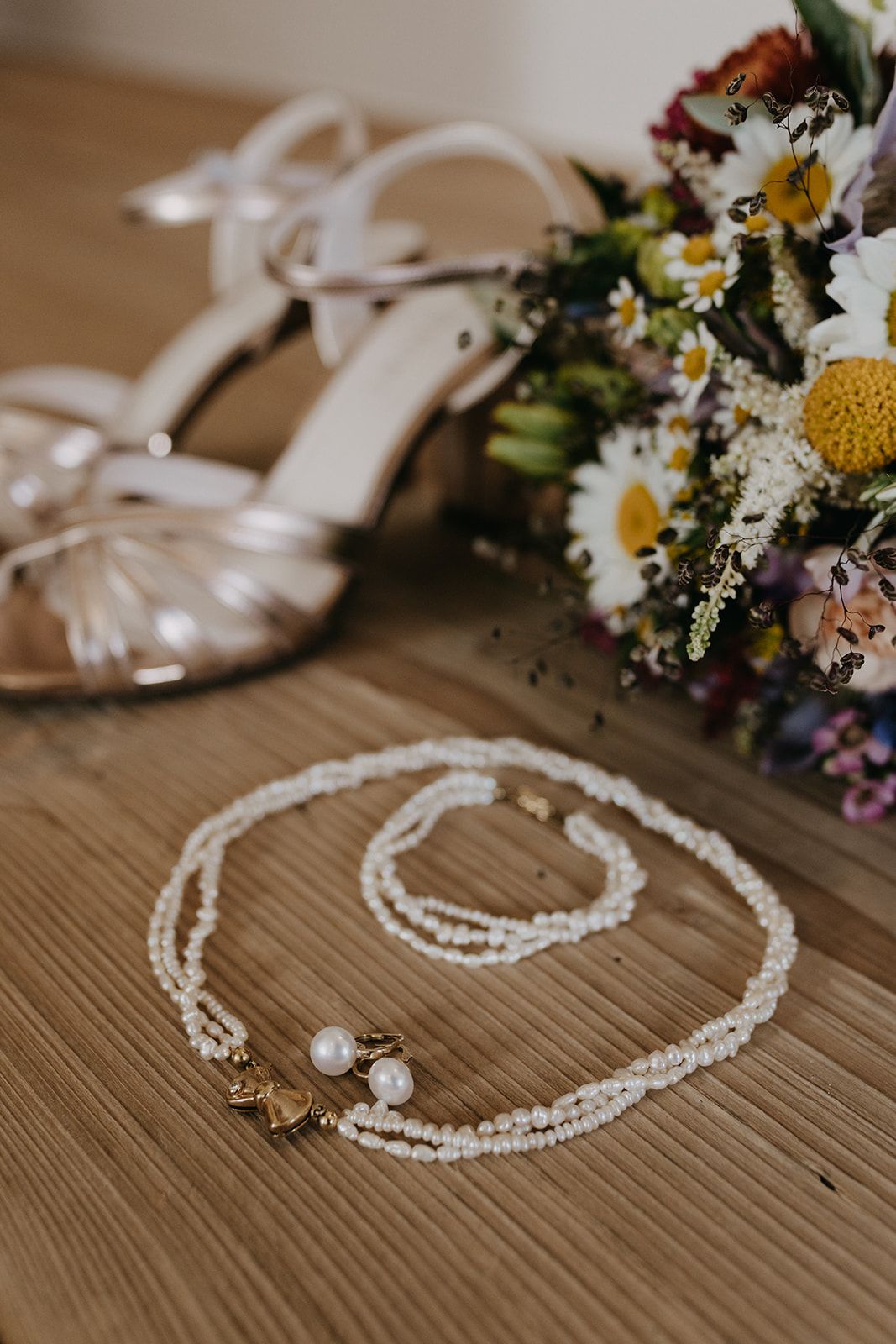 Pearl necklace and bracelet beside bridal heels and colorful wildflower bouquet.