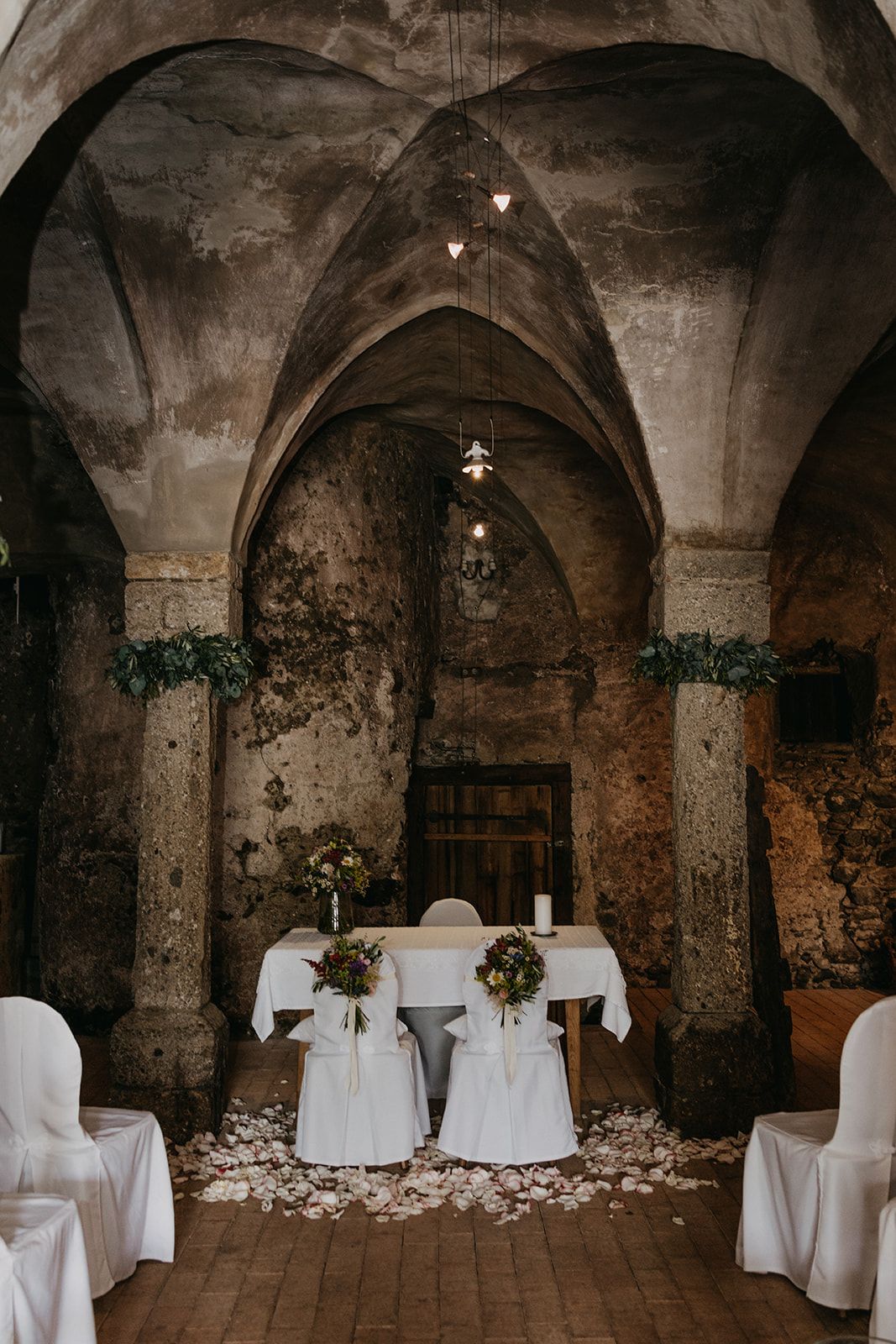 Elegant rustic wedding ceremony setup inside a historic stone vaulted chapel with floral decor.
