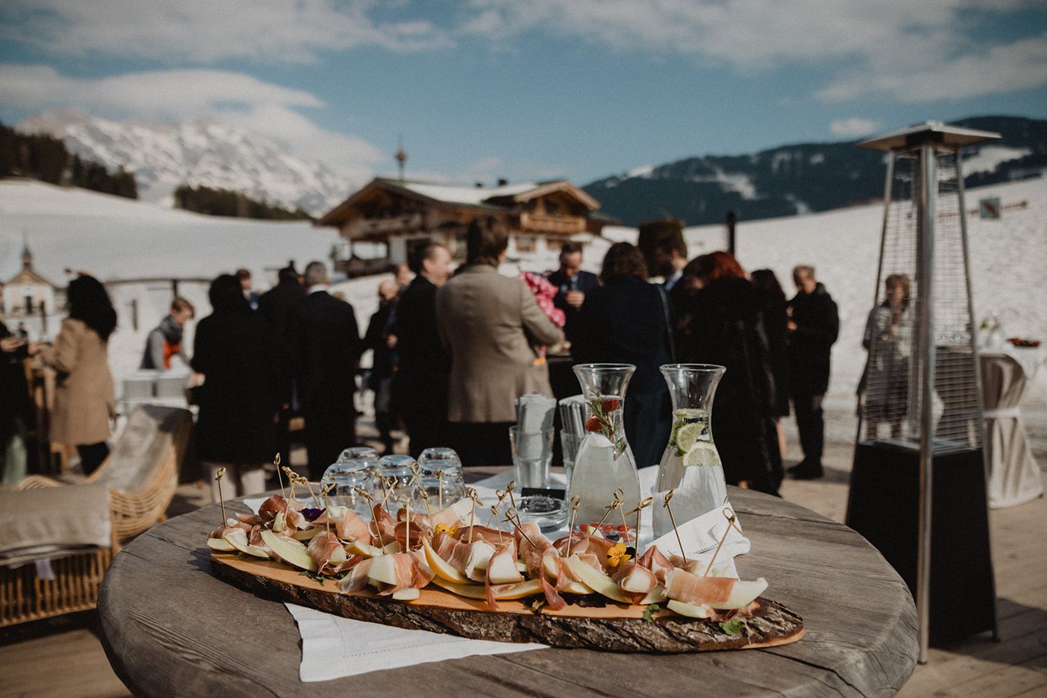 Winter wedding cocktail hour with guests mingling on snowy mountain terrace with appetizers.
