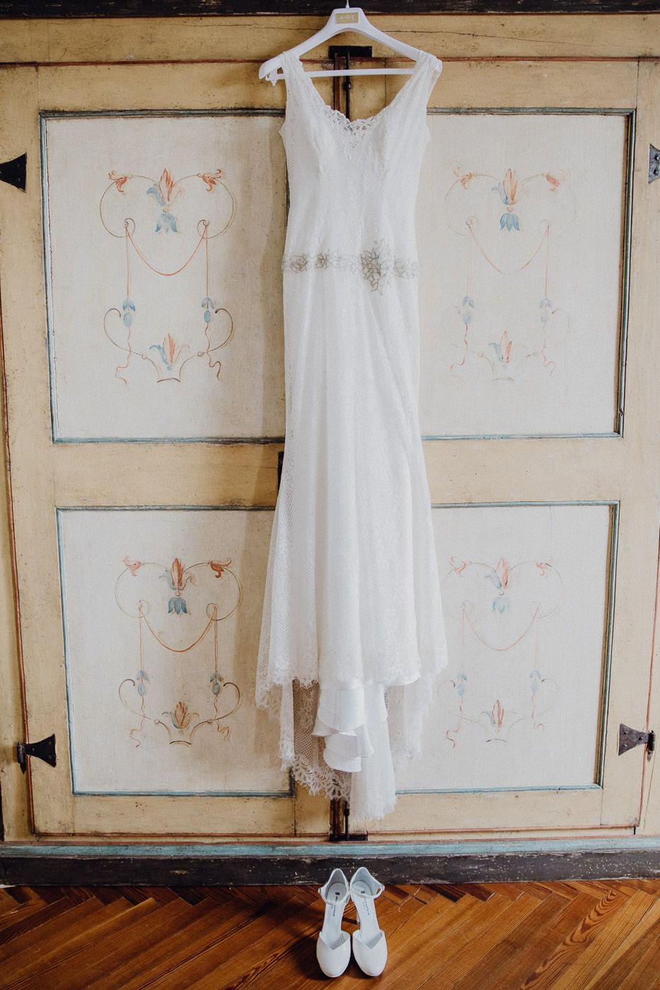 Elegant white wedding dress hanging on an antique painted wardrobe with bridal heels below. Tuscany Villa Catignano