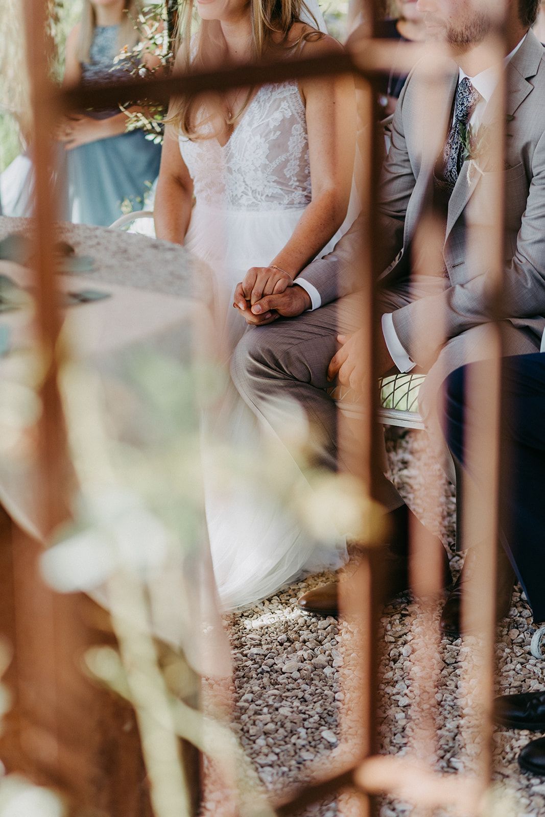 Bride and groom hold hands during outdoor wedding ceremony viewed through decorative iron gate.
