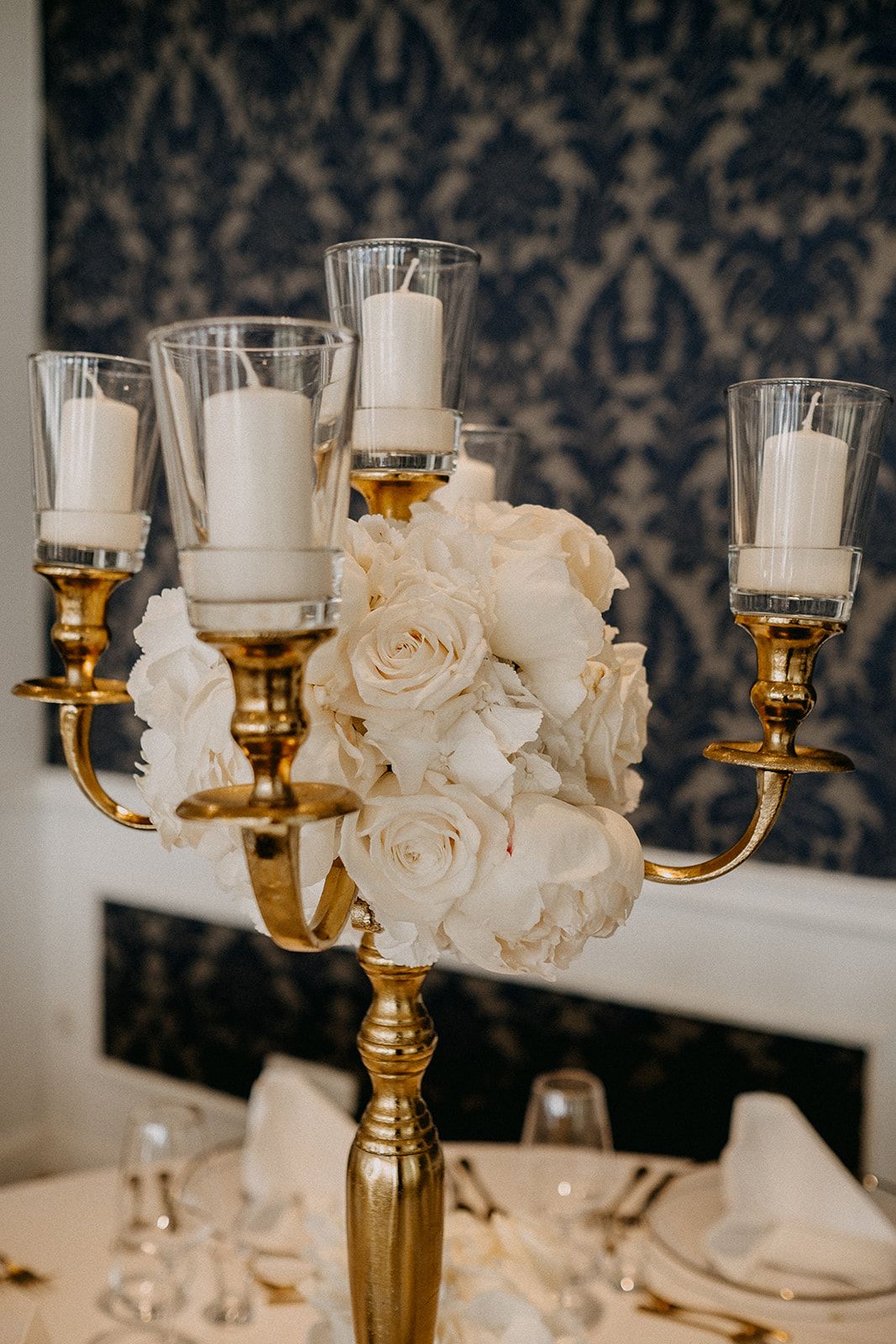Gold candelabra centerpiece with white roses and pillar candles at wedding reception.