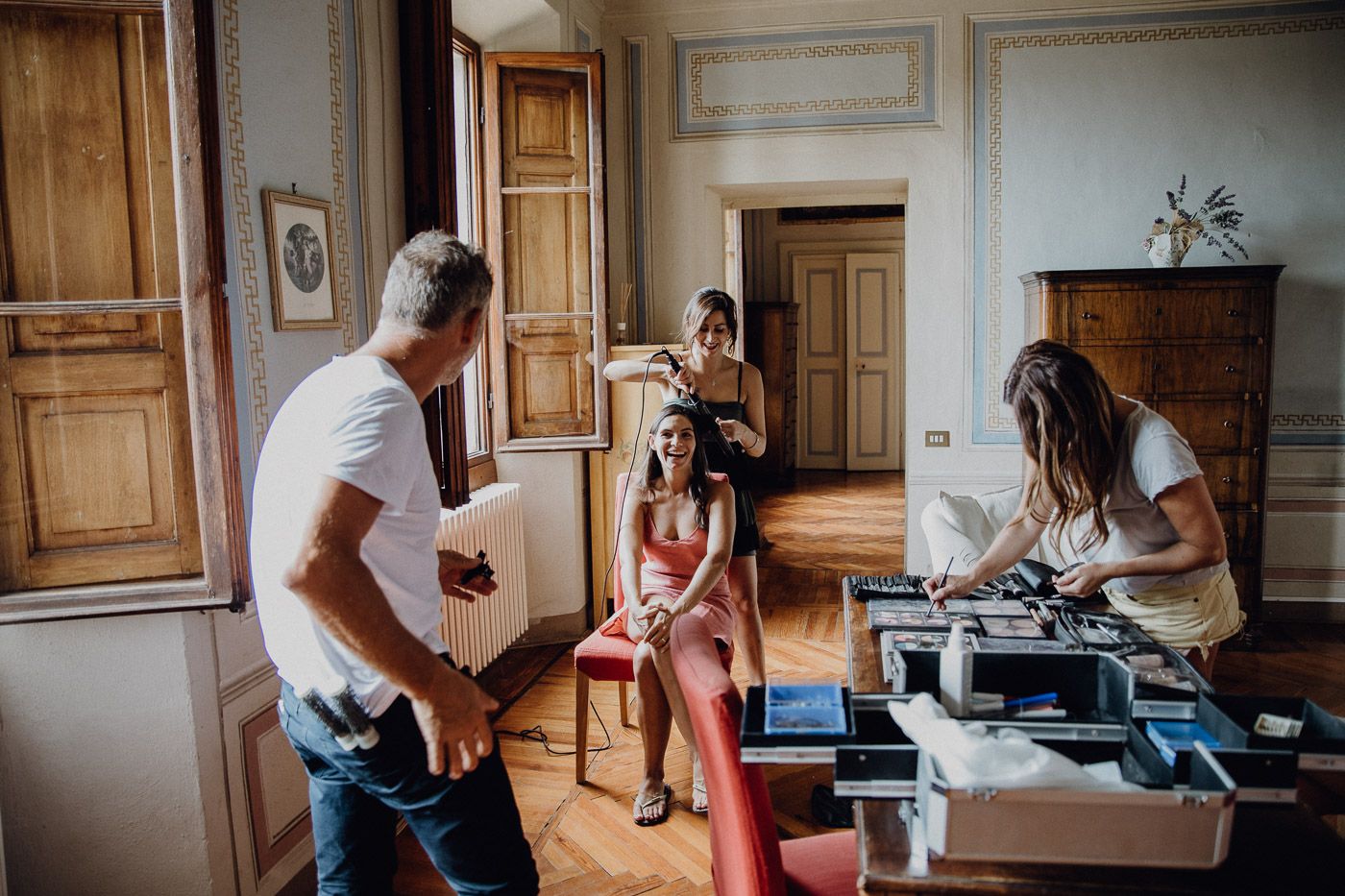 Bride getting hair and makeup done by stylists in an elegant vintage room before her wedding. Tuscany Villa Catignano