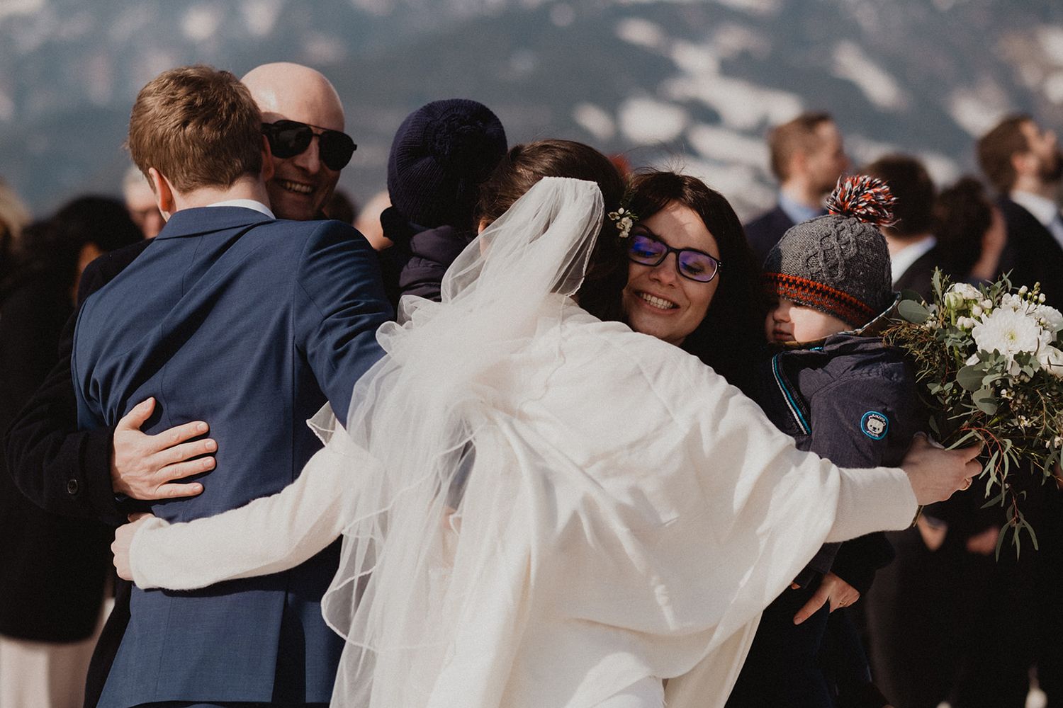 Bride and groom embracing wedding guests outdoors in snowy mountain winter wedding setting. Jufenalm