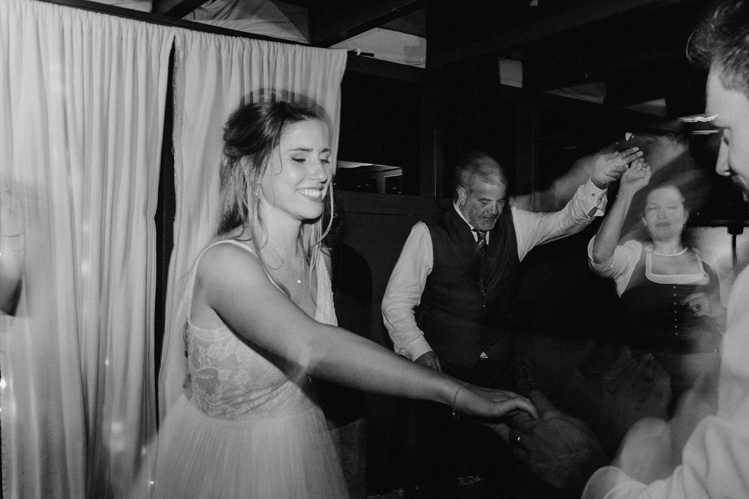 Smiling bride in a lace gown dances joyfully with guests at the wedding reception.