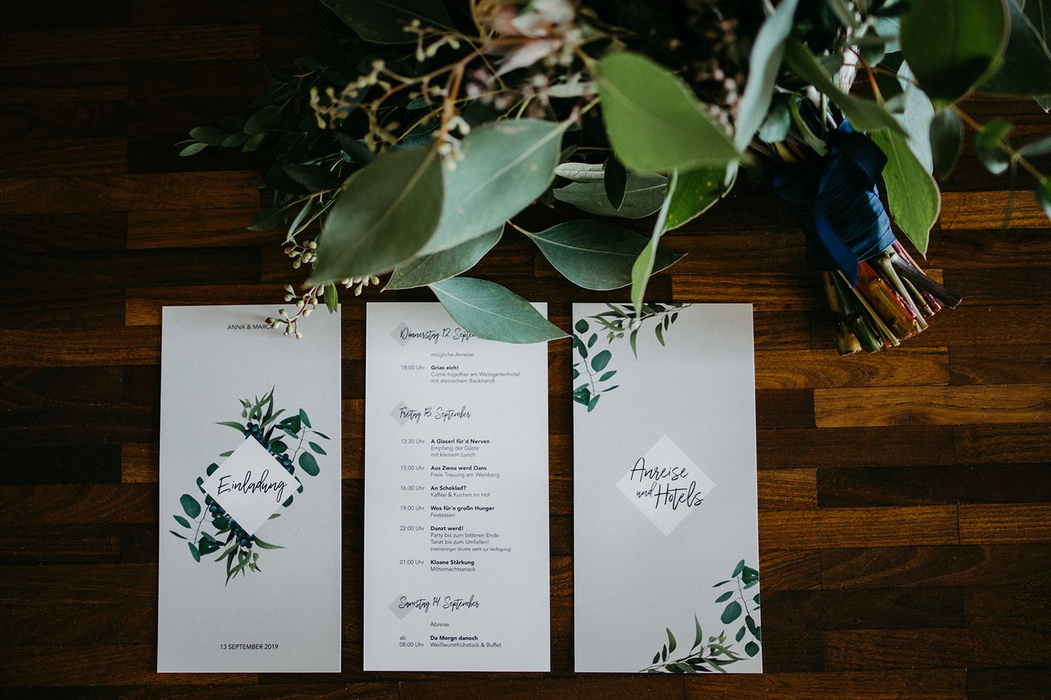 Elegant botanical wedding stationery suite with greenery design laid flat on wooden surface.