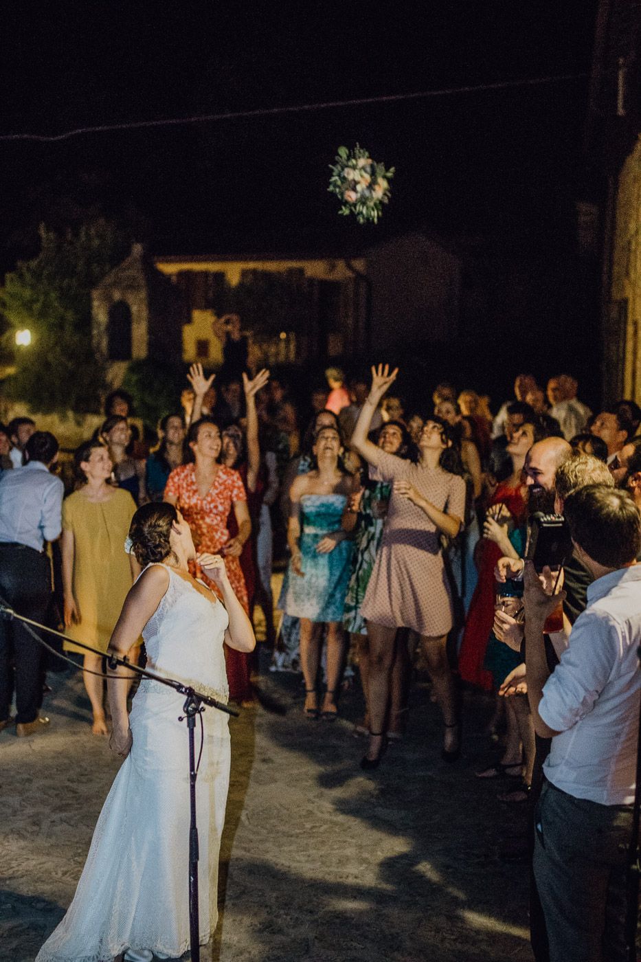 Bride tossing wedding bouquet to excited crowd of guests at outdoor evening wedding reception. Tuscany Villa Catignano