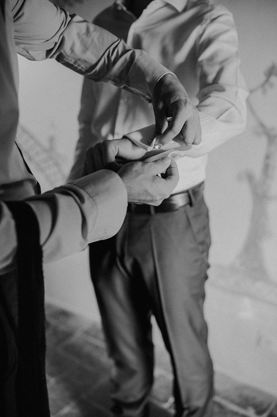 Black and white close-up of groomsmen helping fasten cufflinks during wedding day preparations. Tuscany Villa Catignano