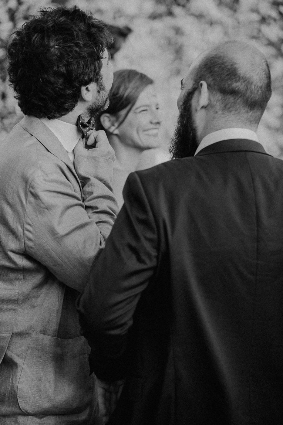Black and white candid photo of wedding guests laughing and conversing at outdoor reception. Tuscany Villa Catignano