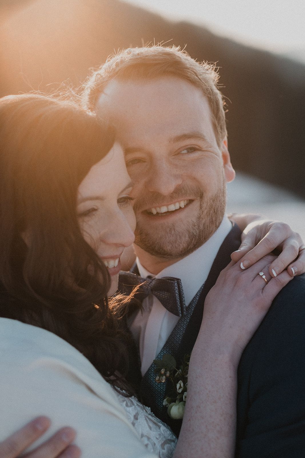 Happy wedding couple embracing at golden hour sunset, groom smiling with bride leaning on his shoulder. Jufenalm