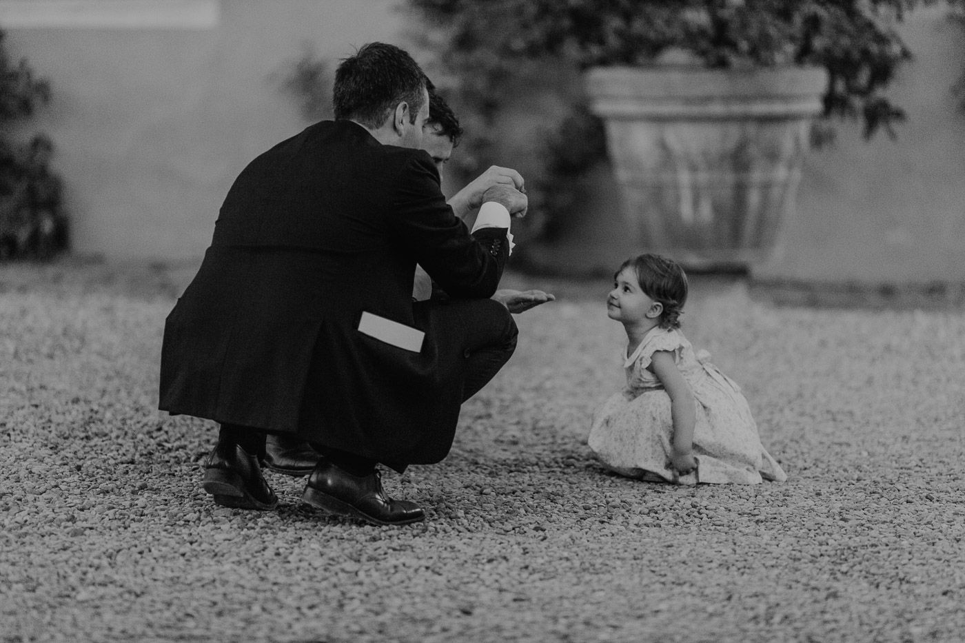 Man in suit crouching to interact with young child at outdoor wedding venue. Tuscany Villa Catignano