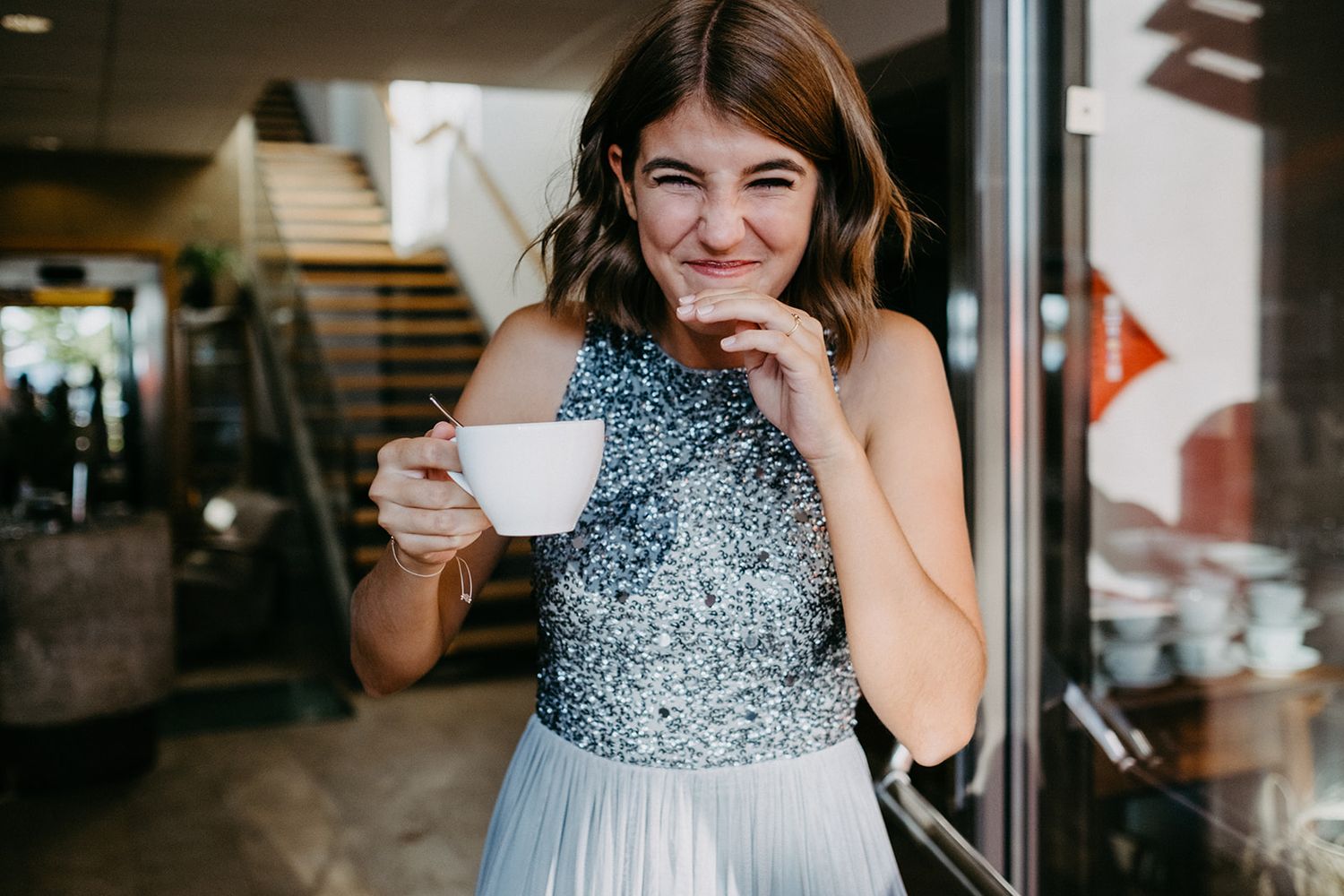 Smiling bridesmaid in silver sequin and blue tulle dress holding a white teacup at a wedding venue.