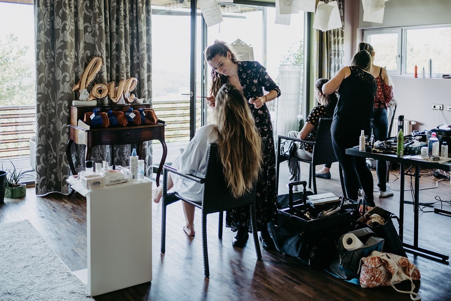 Wedding hair stylist preparing bride's long hair in a modern salon with love sign decor.